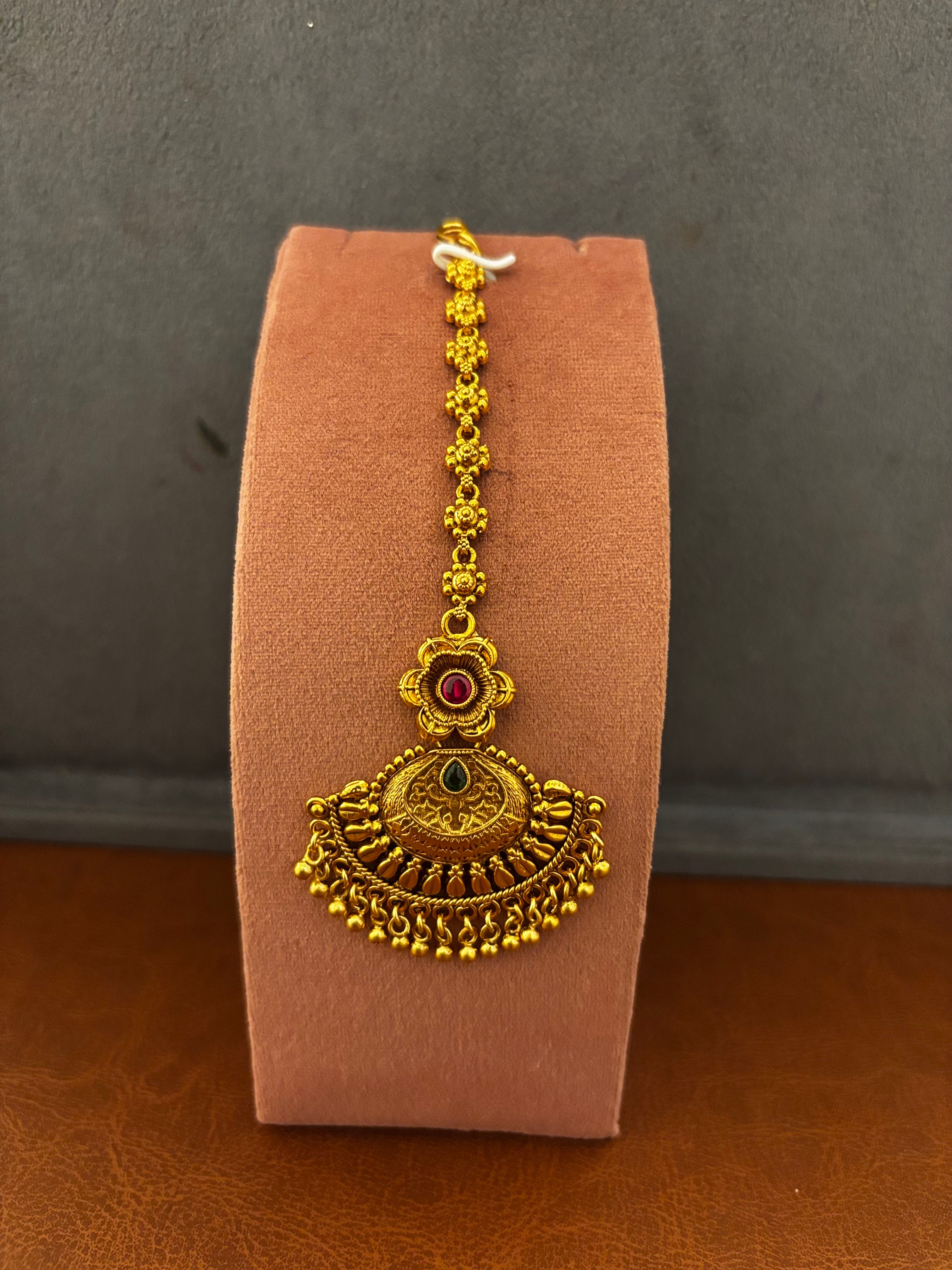 Gold pendant with red and green gemstones on a textured brown background