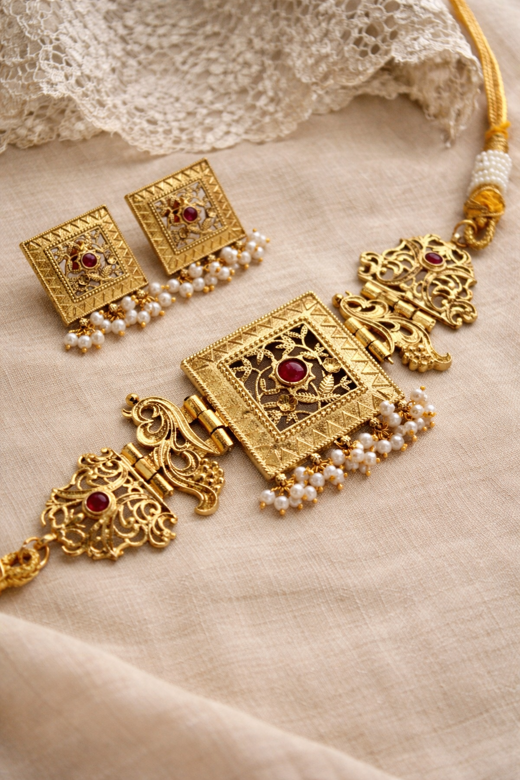 Gold jewelry set with red stones and pearl strands on a beige fabric background