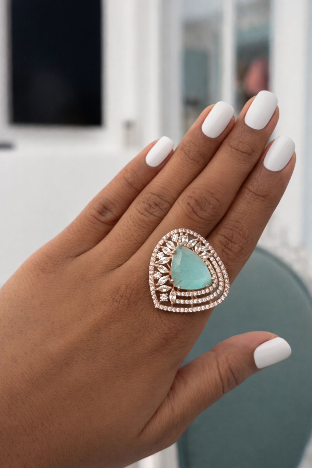 Hand wearing a turquoise ring with a decorative band against a blurred indoor background