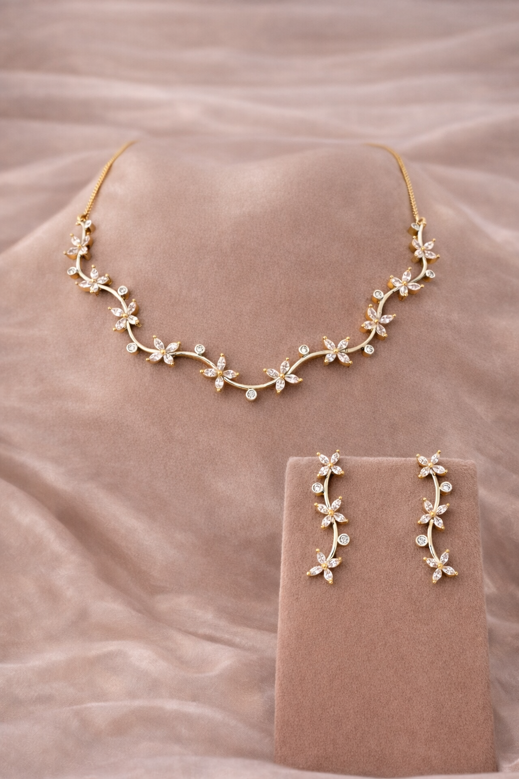 Floral necklace and earrings set on a soft pink fabric background