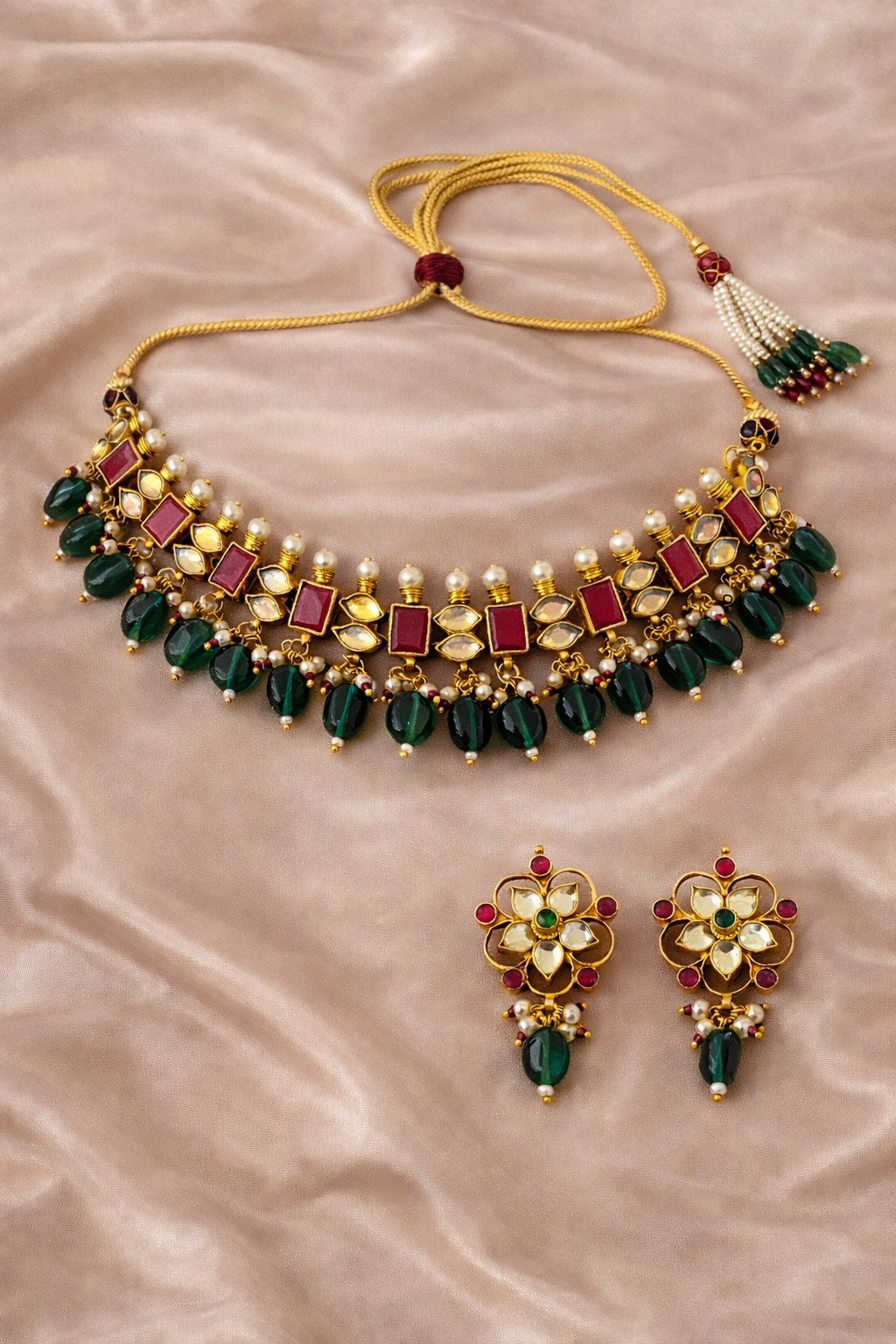 Gold necklace with green and red stones on a beige fabric background