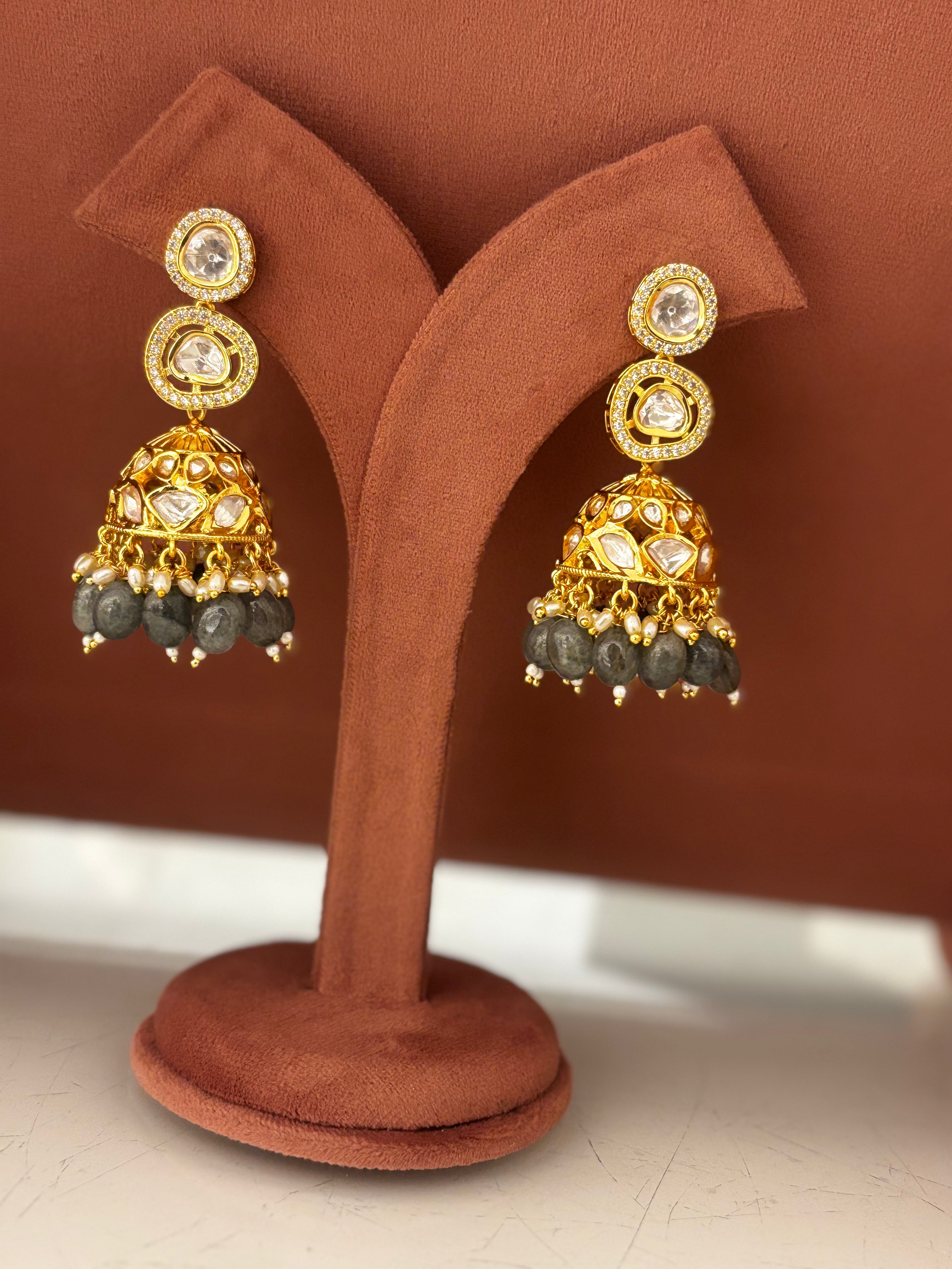 Gold and green beaded earrings on a white fabric background