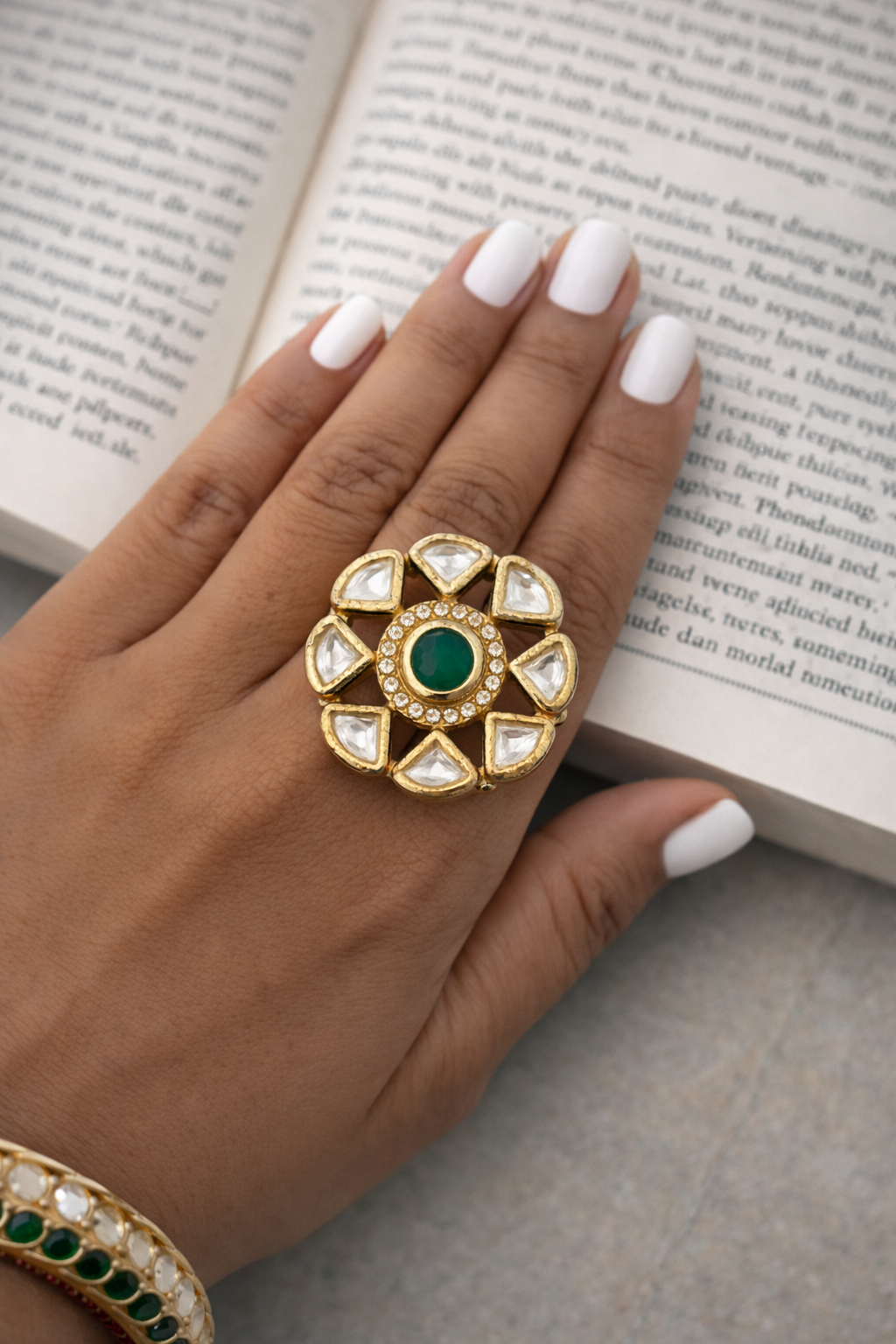 Hand wearing a decorative ring with emerald green gemstone on an open book background