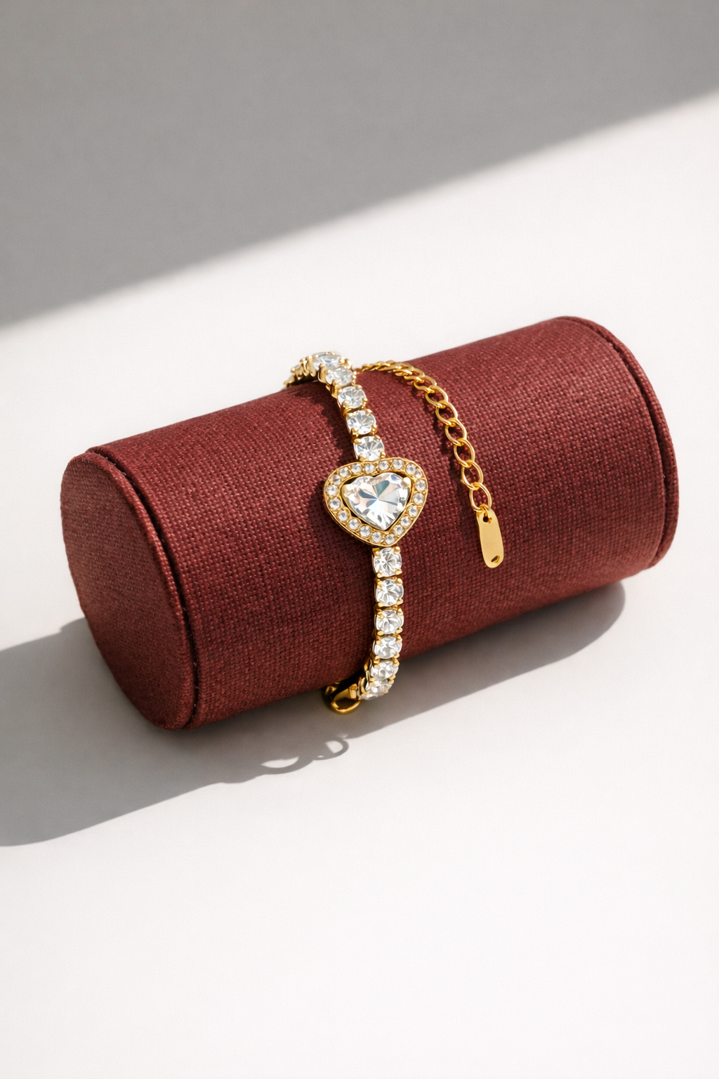 Gold bracelet with heart-shaped clasp on a red jewelry roll against a light background