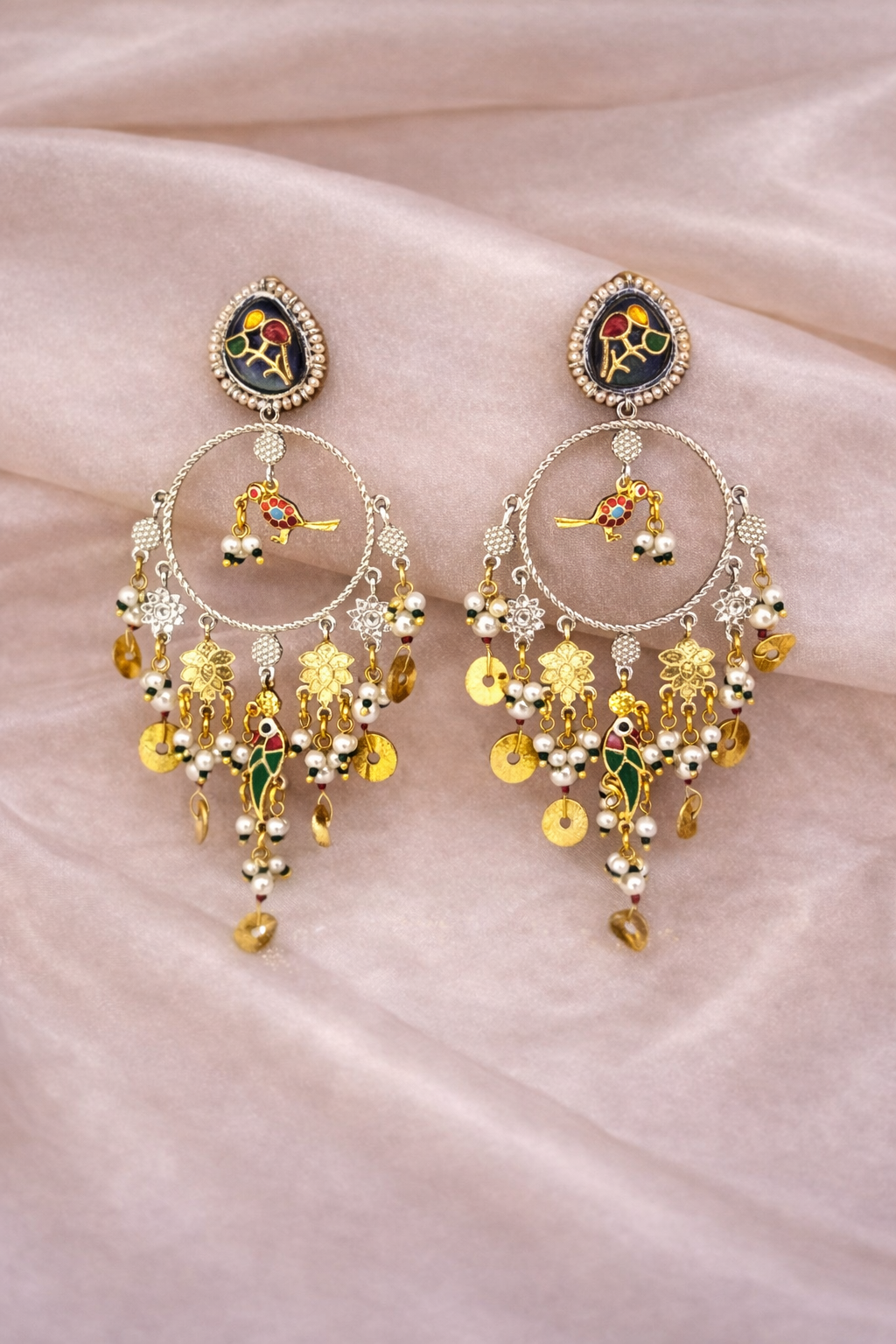 Ornate gold and multicolored earrings on a soft pink fabric background