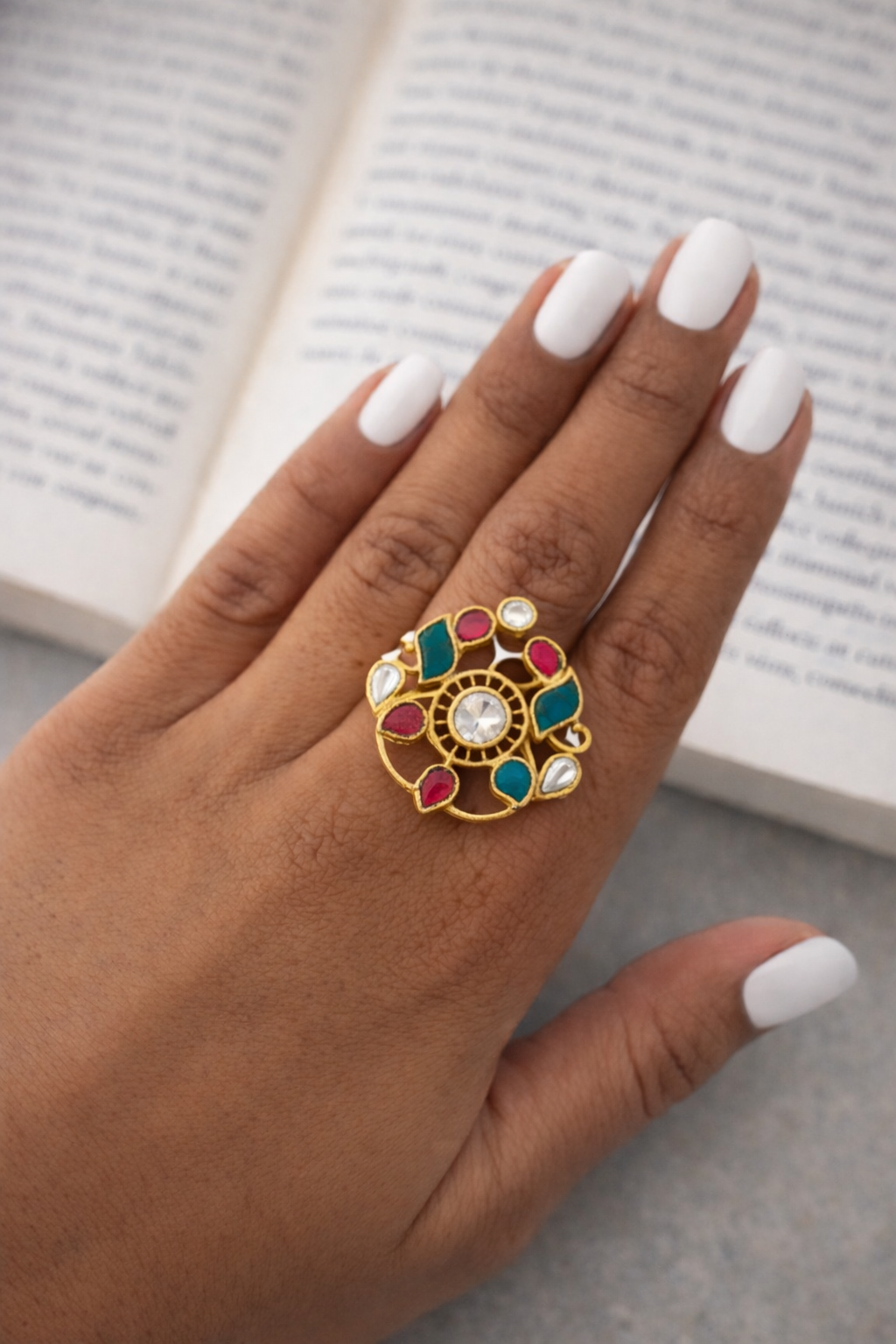 Decorative ring with colorful gemstones on a hand against an open book background