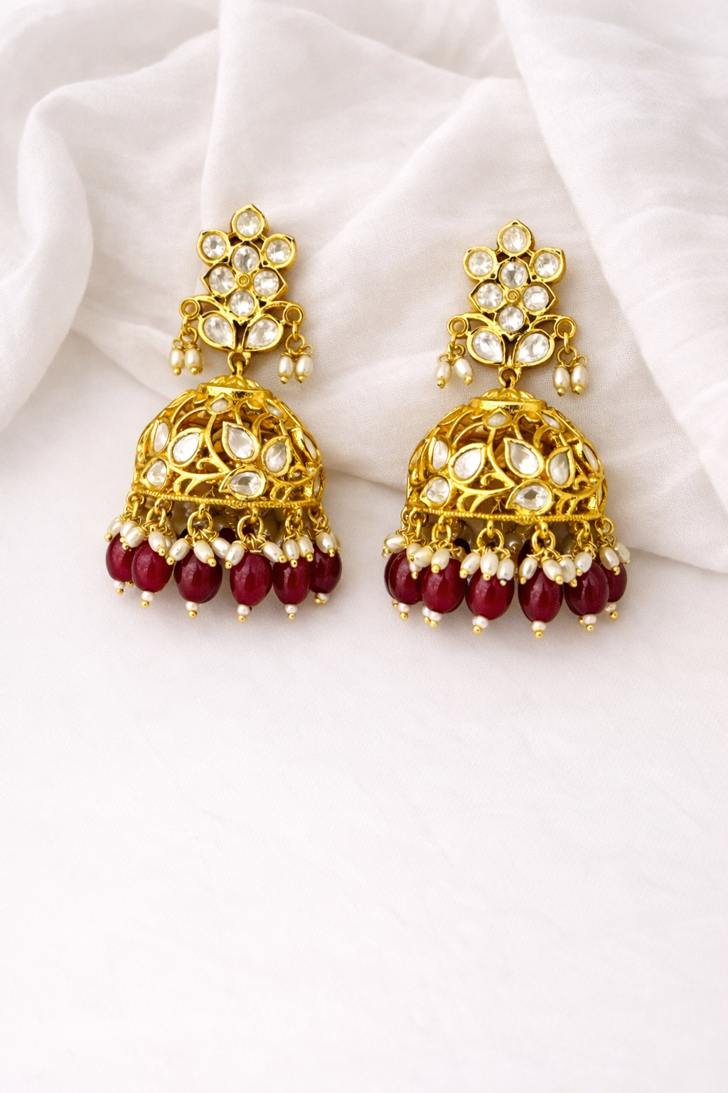 Gold and red earrings on a white fabric background