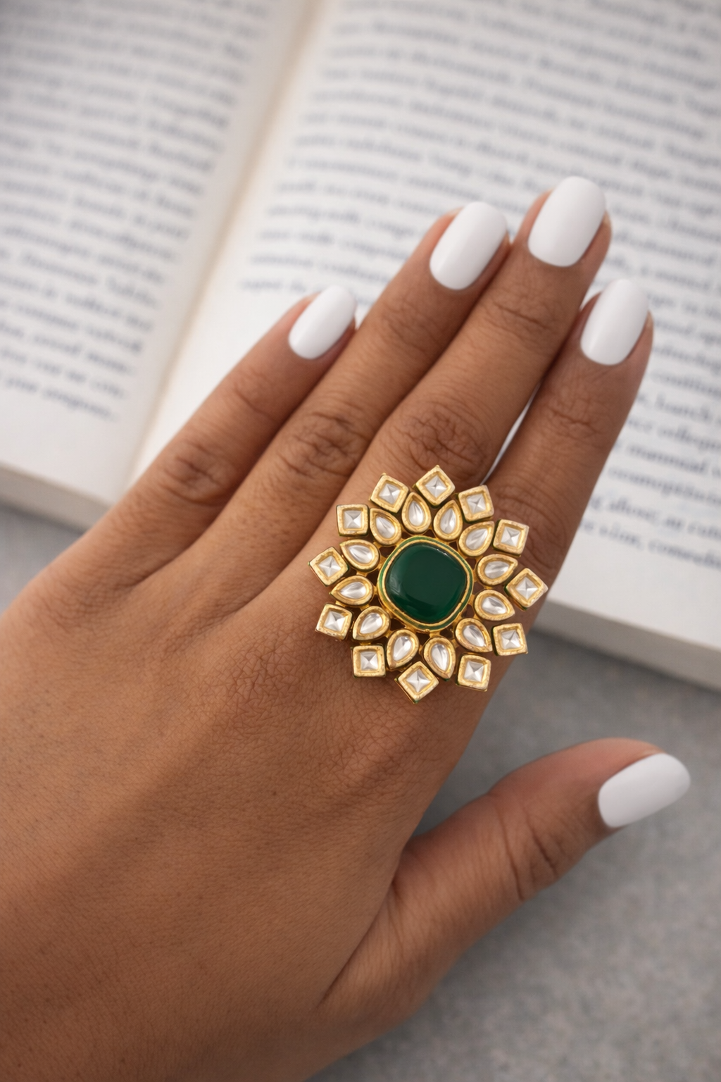 Hand wearing a decorative ring with a green gemstone on a book background