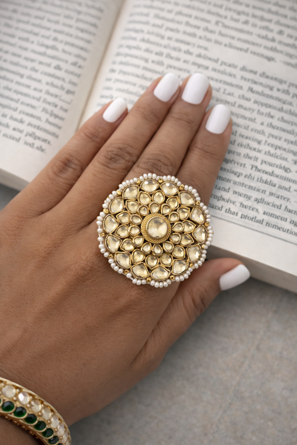 Hand wearing a gold ring with pearls on an open book