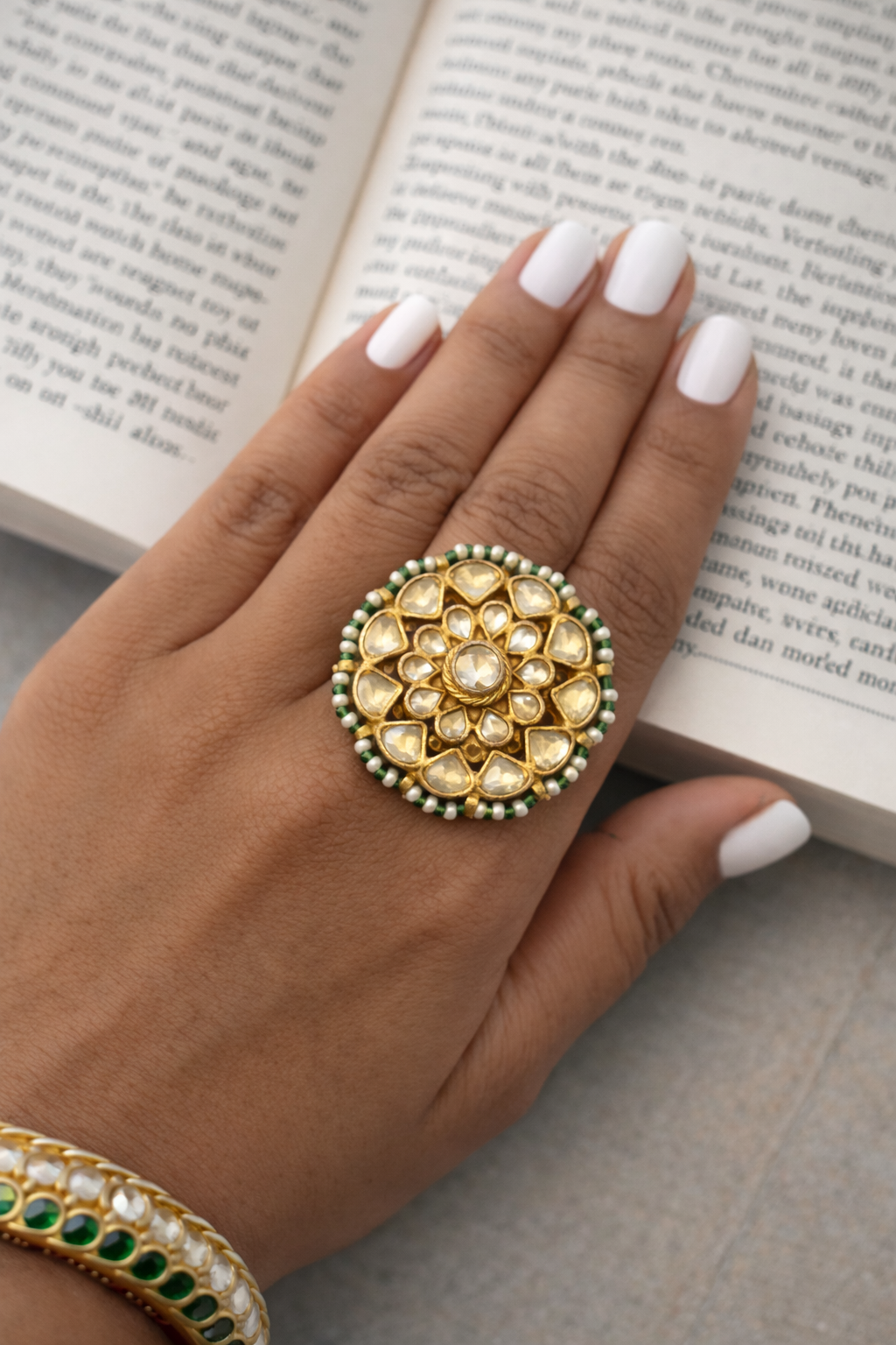 Hand wearing a gold and green ring with an open book in the background