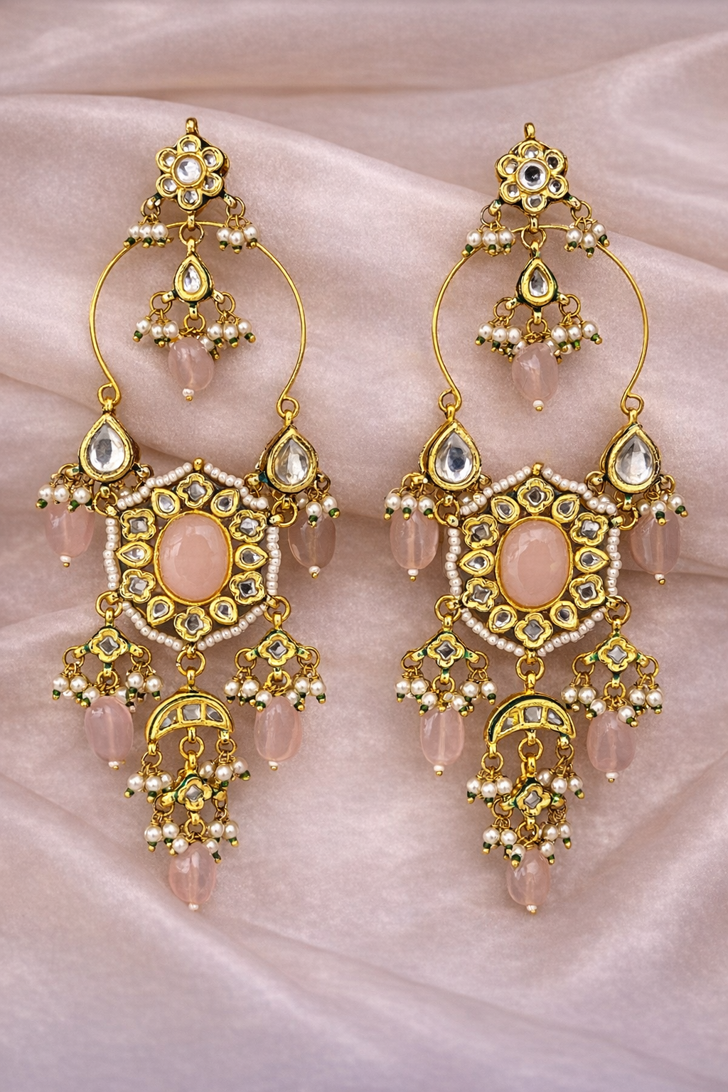 Ornate gold earrings with colorful beads on a pink fabric background