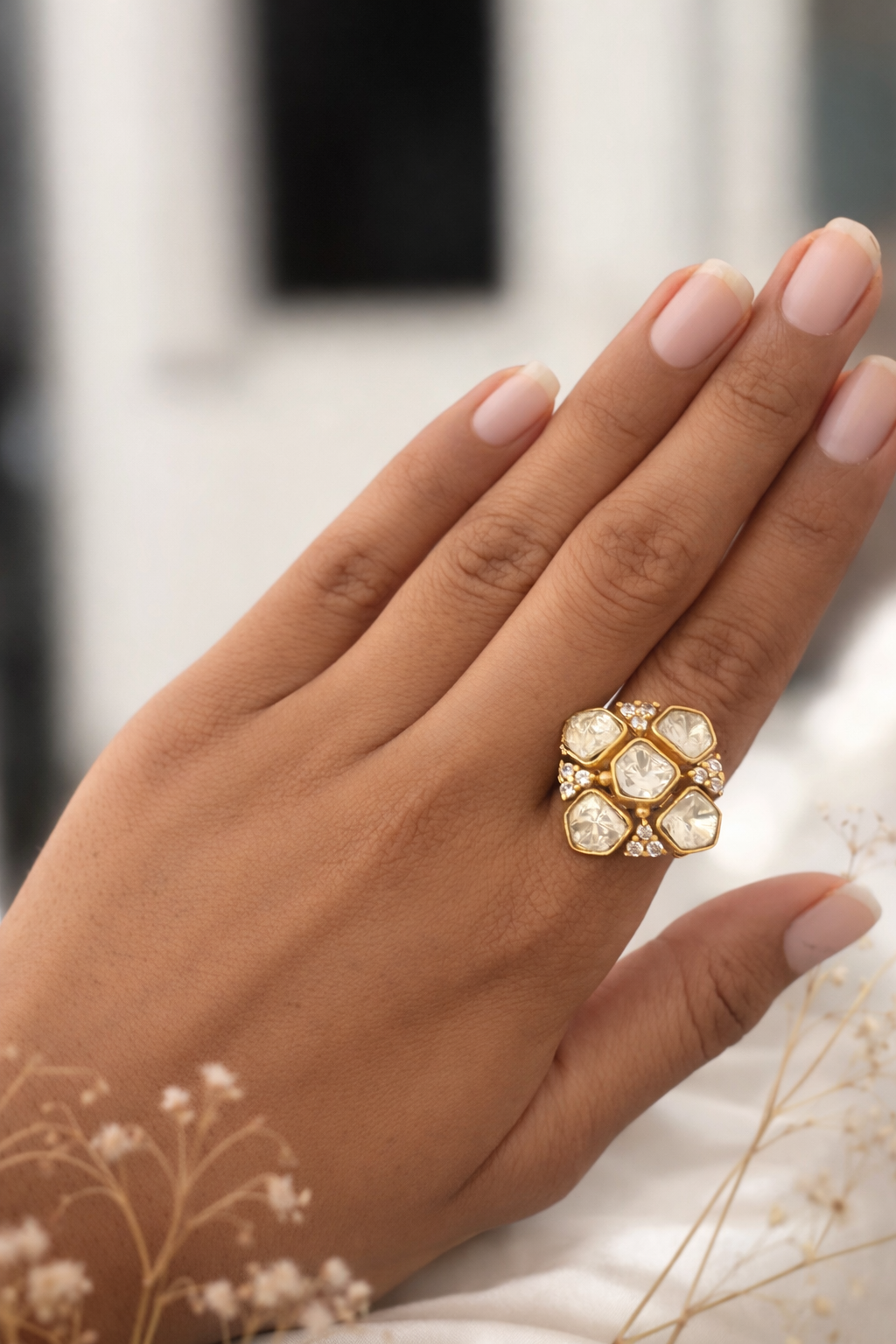 Hand wearing a gold ring with gemstones against a blurred background