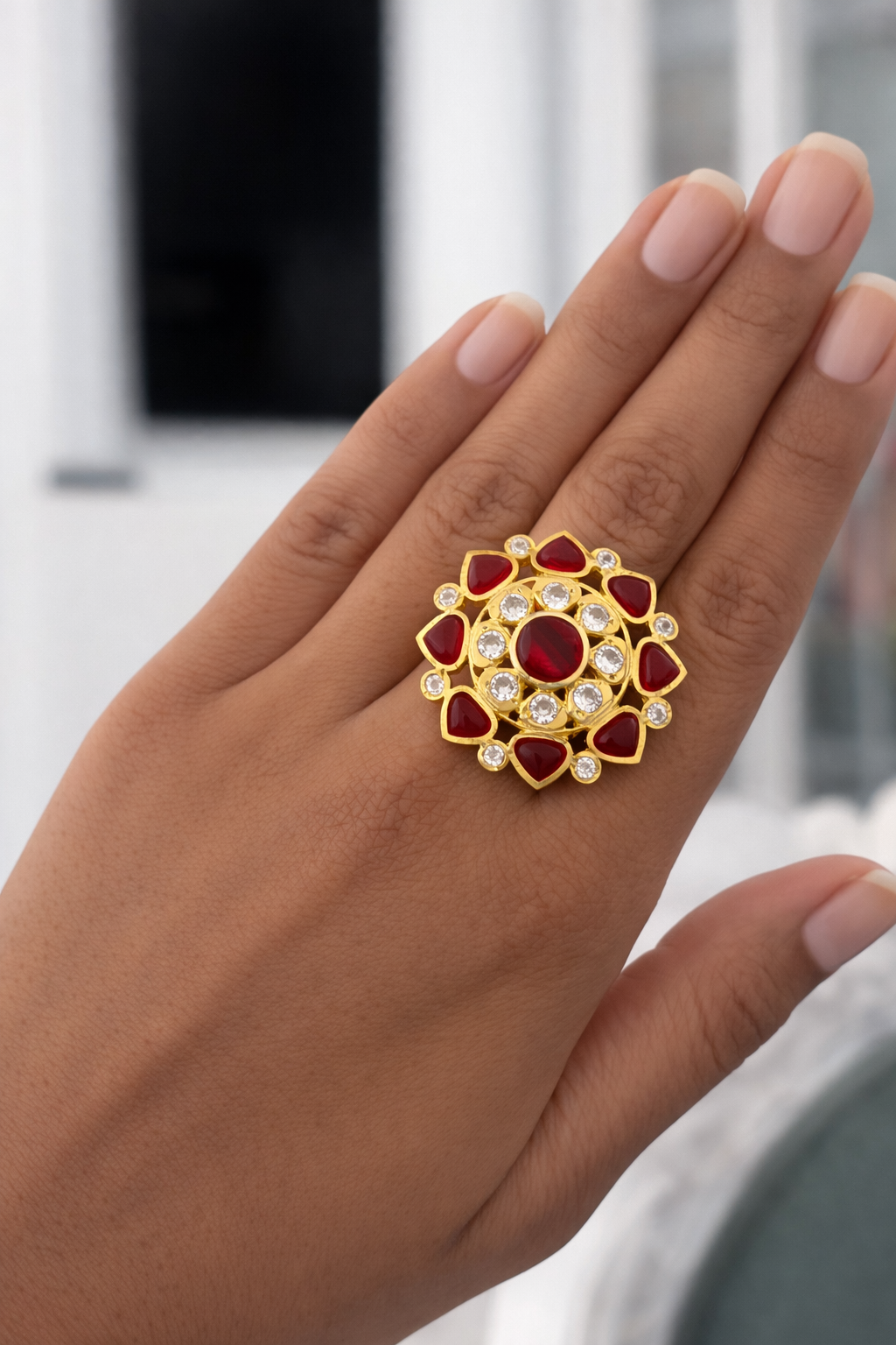 Decorative ring with red gemstones and gold accents on a hand against a blurred background