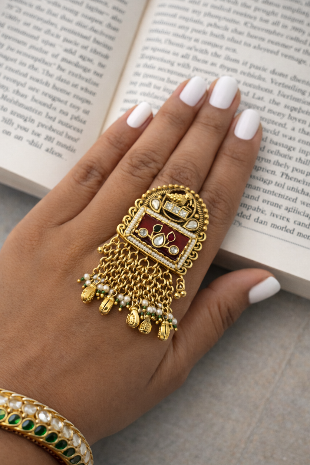 Hand wearing a gold ring with red stone and green gemstones on an open book background