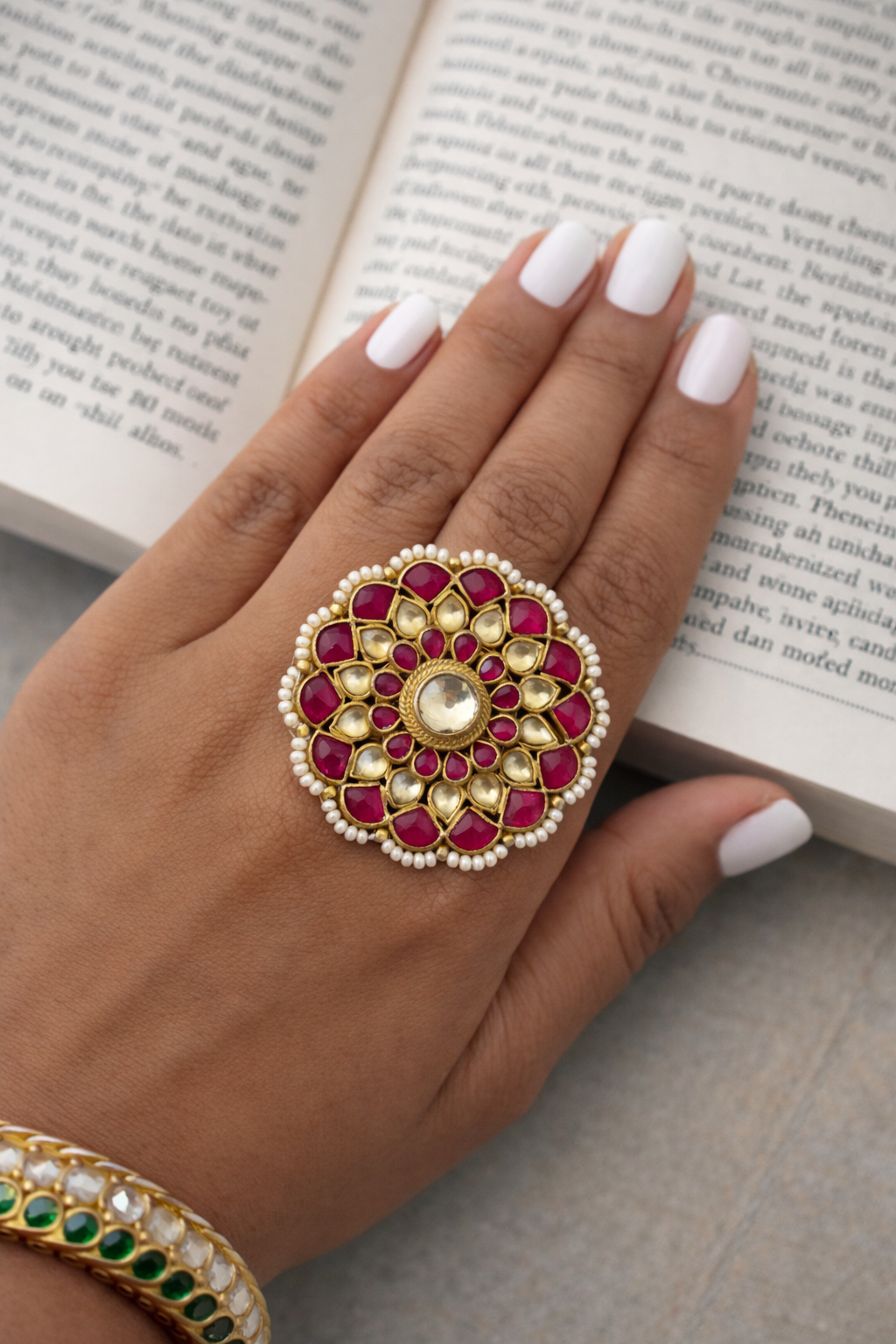 Hand wearing a decorative ring with red stones and gold accents on an open book.