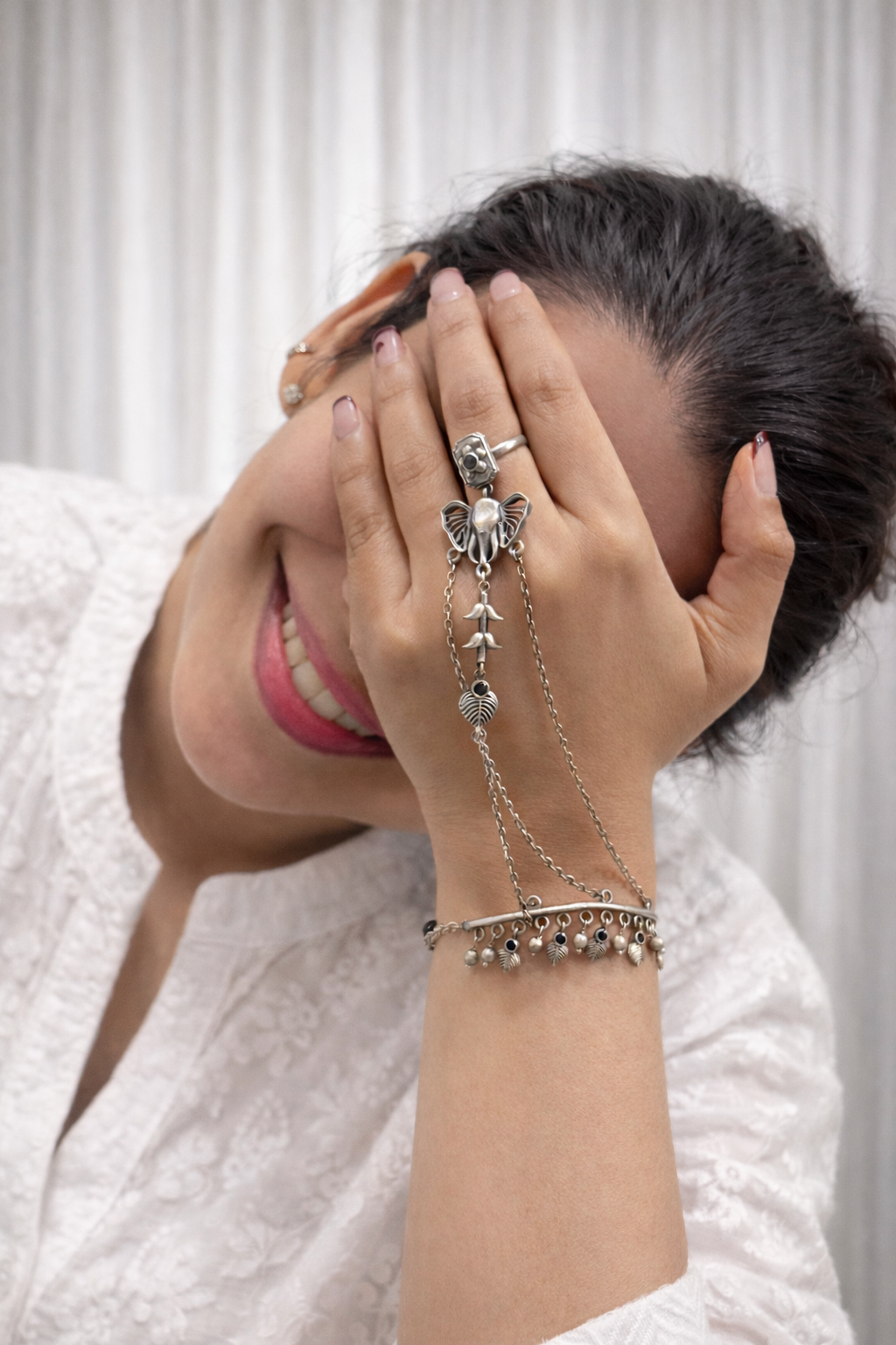 Person wearing multiple silver rings and bracelets on a plain background