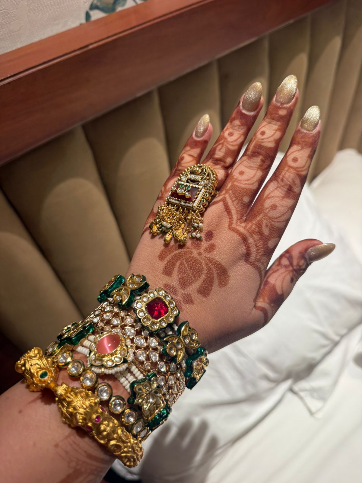 Hand with intricate henna design wearing gold jewelry against a neutral background