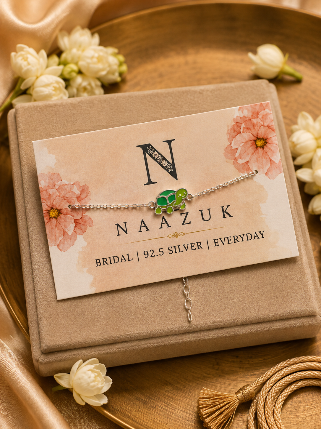 925 Sterling Silver Turtle Rakhi bracelet with a green turtle charm displayed in premium packaging on a jewellery box with jasmine flowers for Raksha Bandhan.