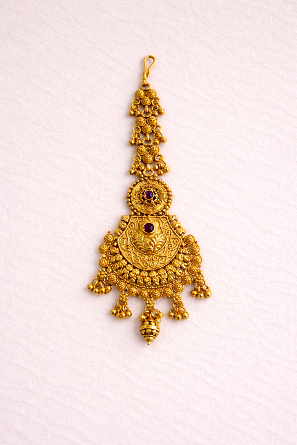 Gold tikka with intricate designs on a light pink background