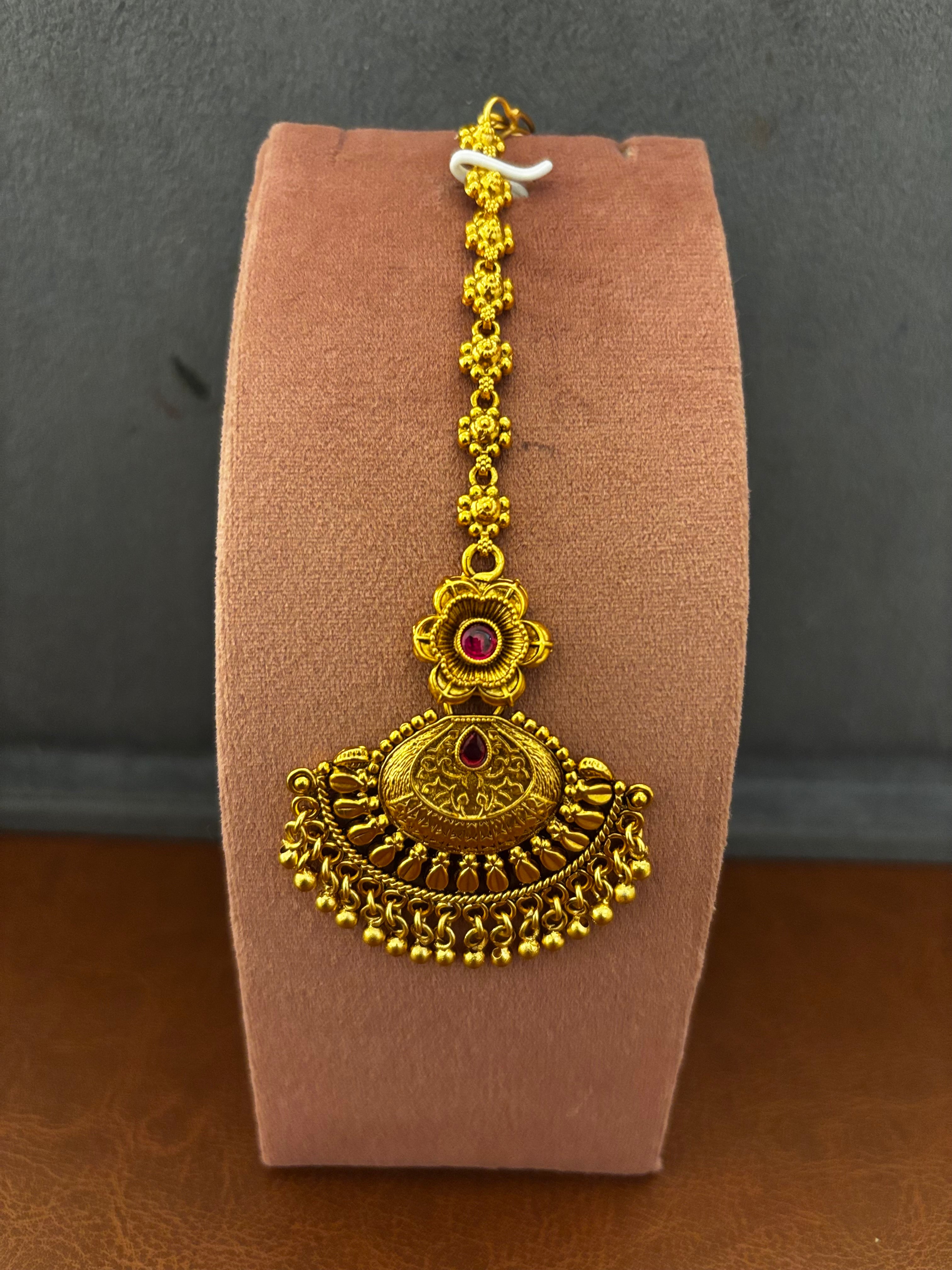Gold necklace with a red gemstone on a brown velvet cushion against a gray background