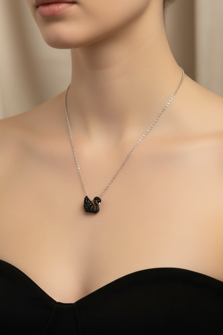 A delicate silver necklace with a black swan pendant, styled on draped champagne-colored satin fabric with dried baby's breath flowers.