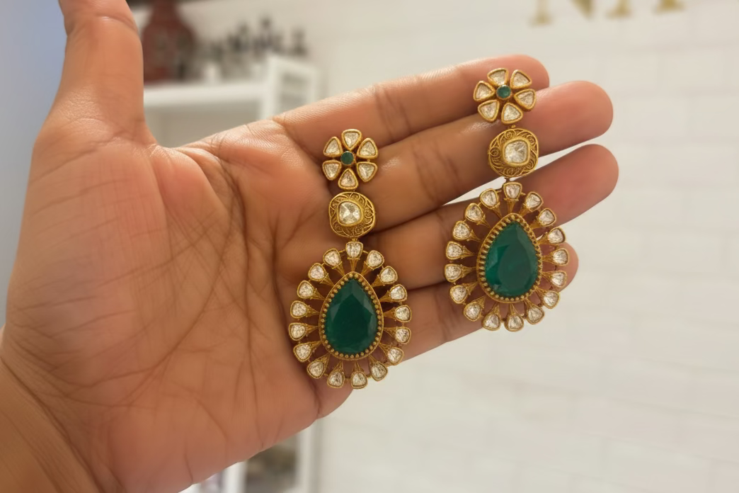 Gold and green earrings held in a hand with a blurred background