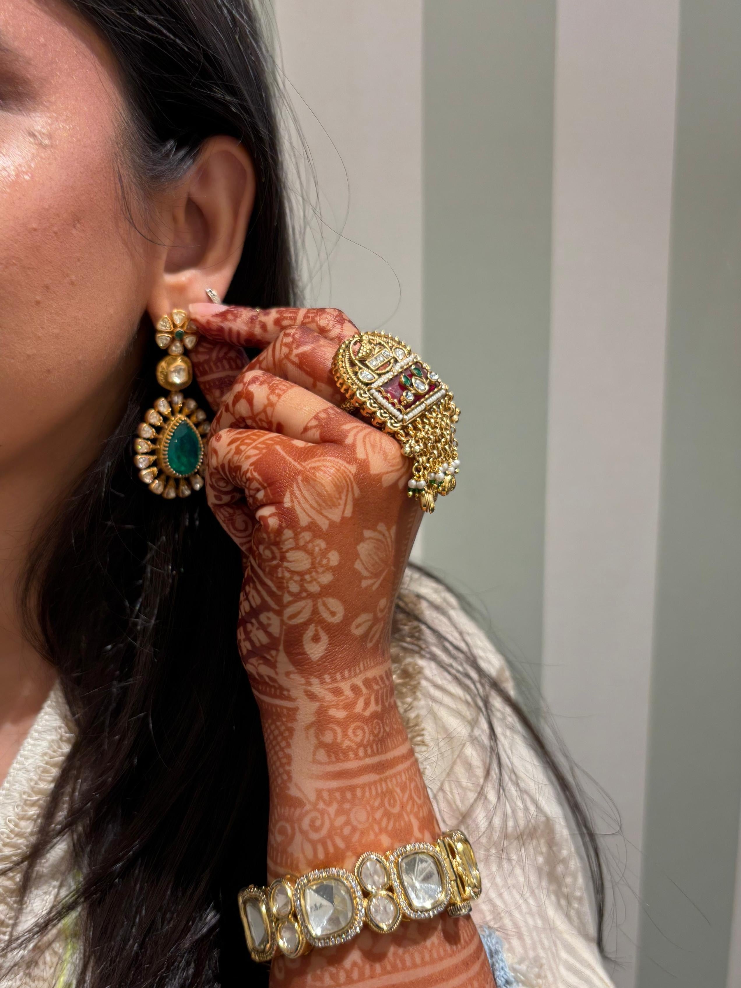 Woman wearing gold earrings and bangles with intricate henna designs on her arm.
