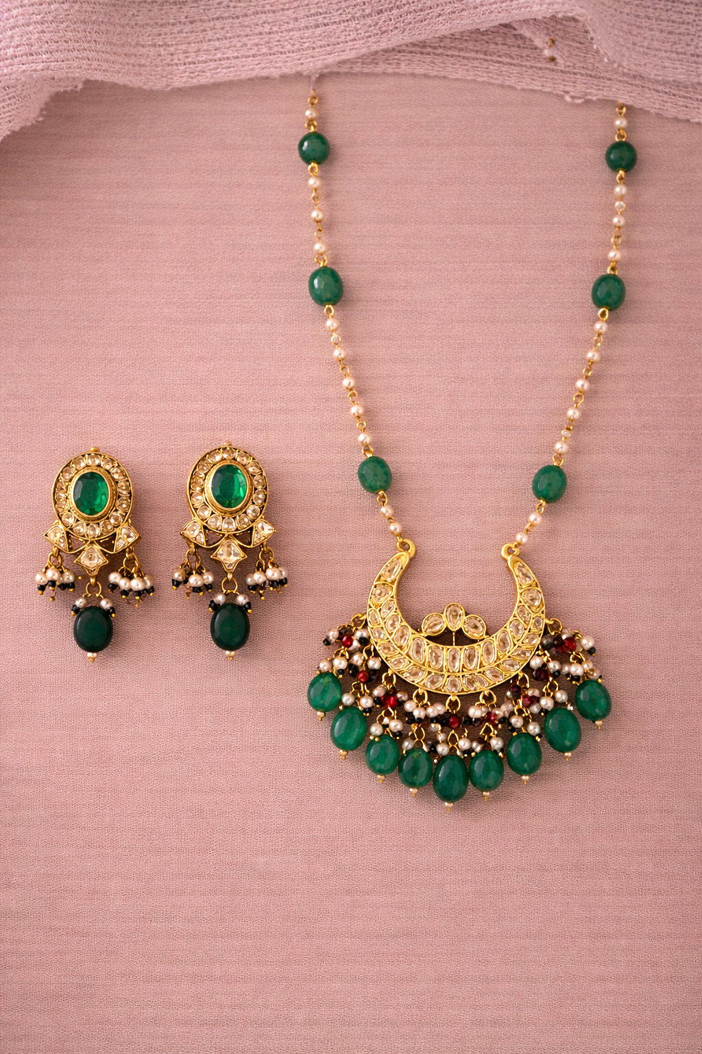 Gold necklace with green beads and matching earrings on a pink fabric background