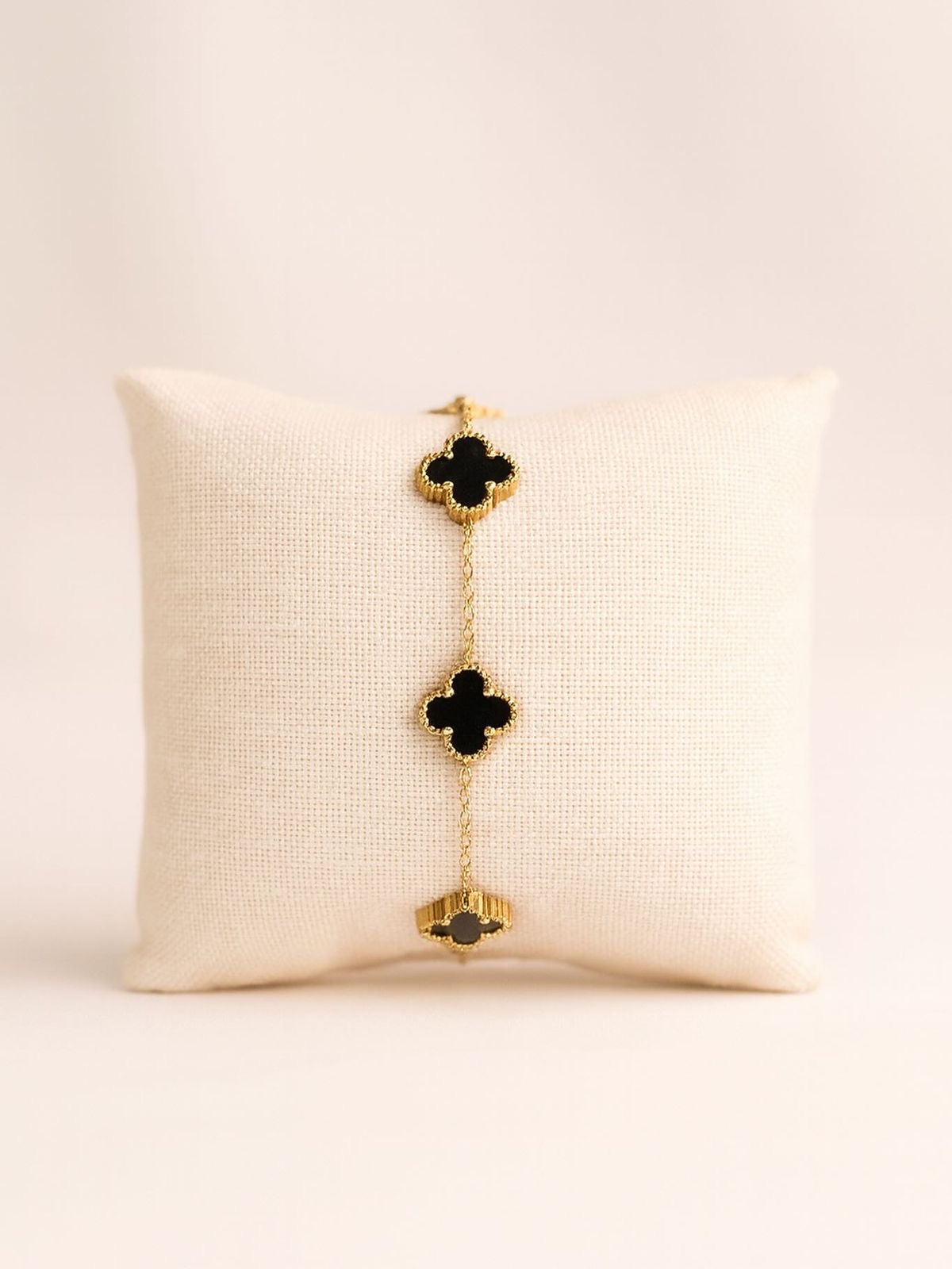 Gold bracelet with black clover-shaped charms on a beige pillow