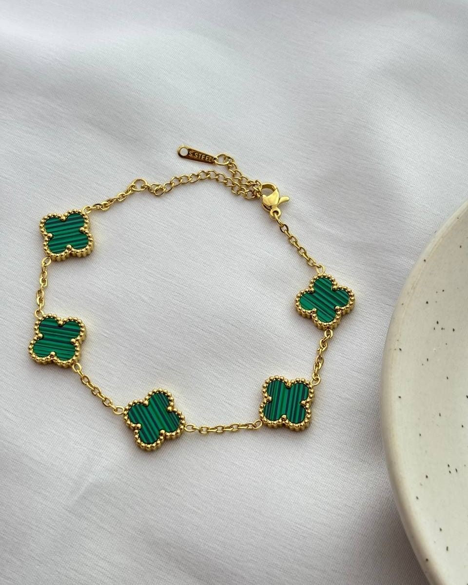 Gold bracelet with green clover-shaped charms on a white surface.