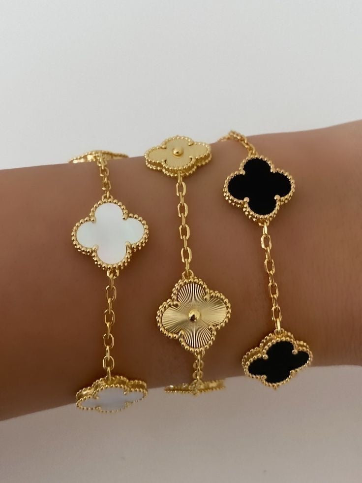 Gold bracelet with clover-shaped charms on a wrist against a neutral background