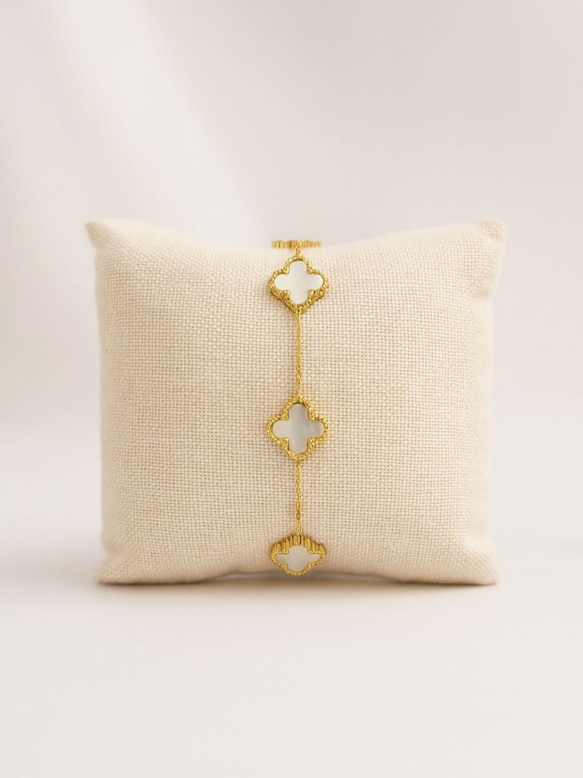 Gold bracelet with clover-shaped links on a textured beige pillow against a light background