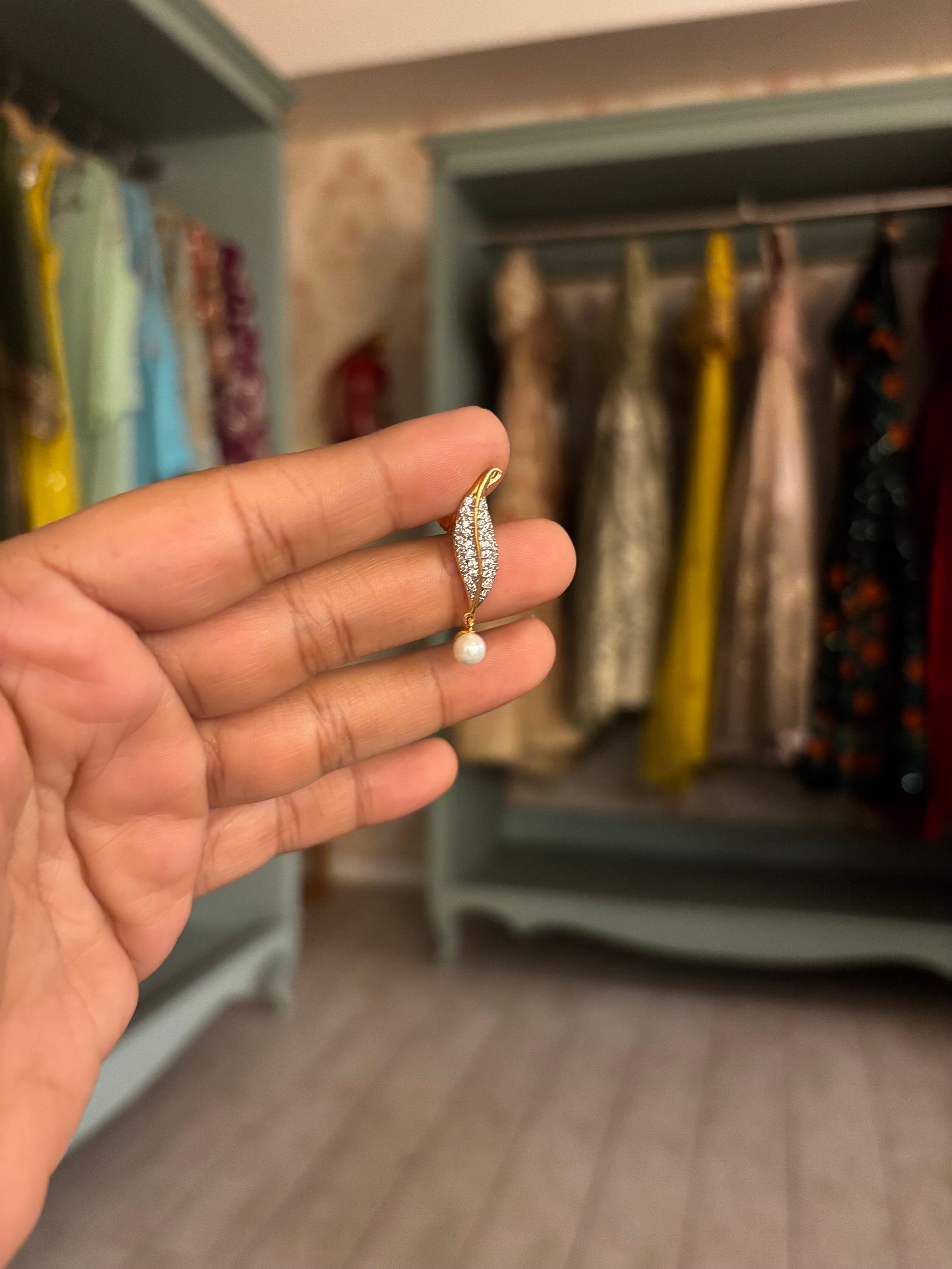 Gold-finish crystal tennis necklace featuring a leaf-inspired pearl pendant with matching crystal and pearl earrings displayed on a textured beige background.