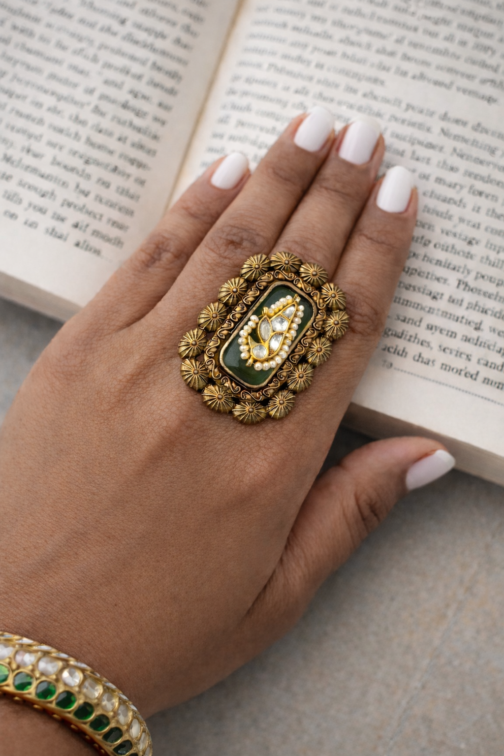 Hand wearing a decorative gold ring with a green gemstone on an open book