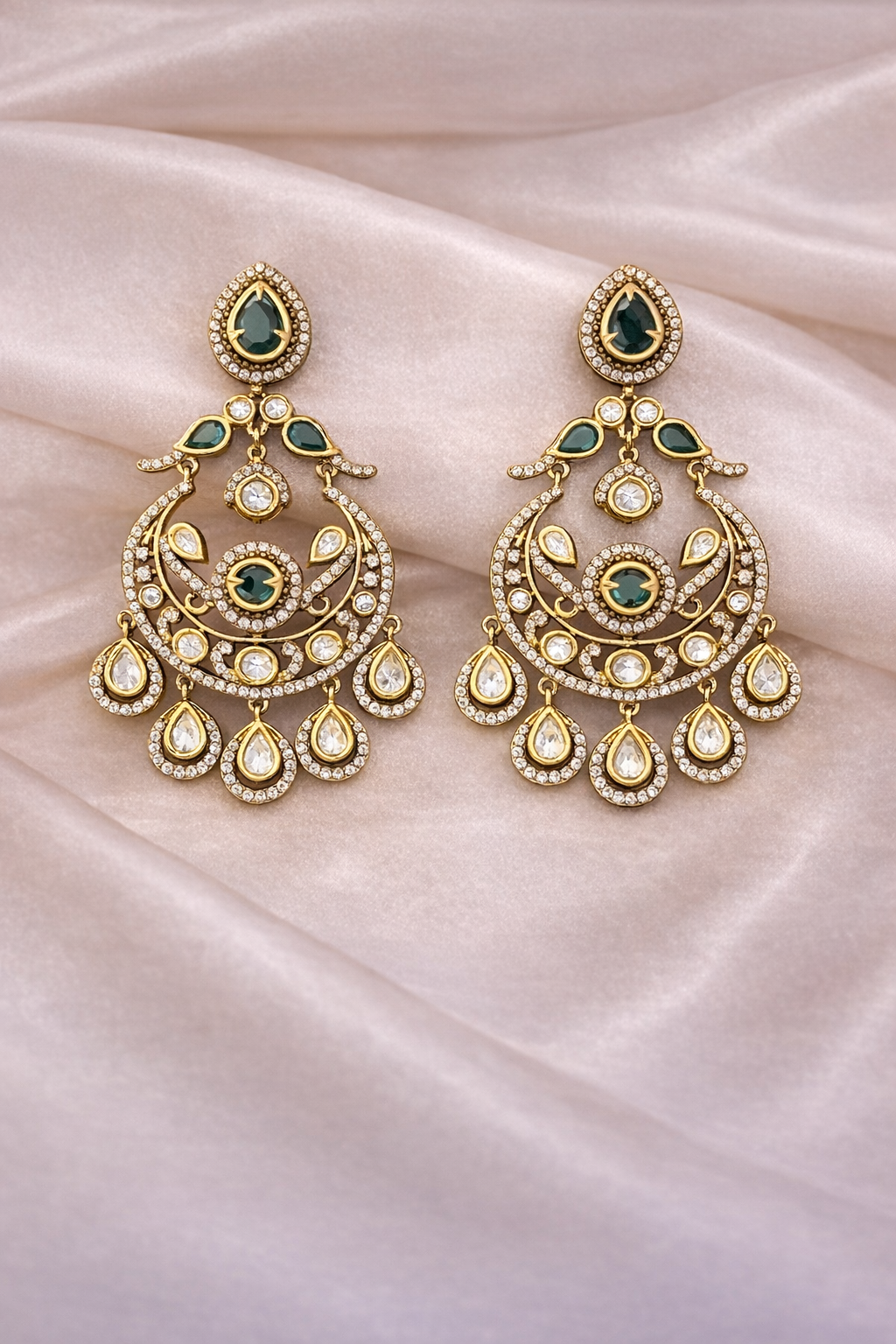 Ornate gold earrings with green gemstones on a pink fabric background