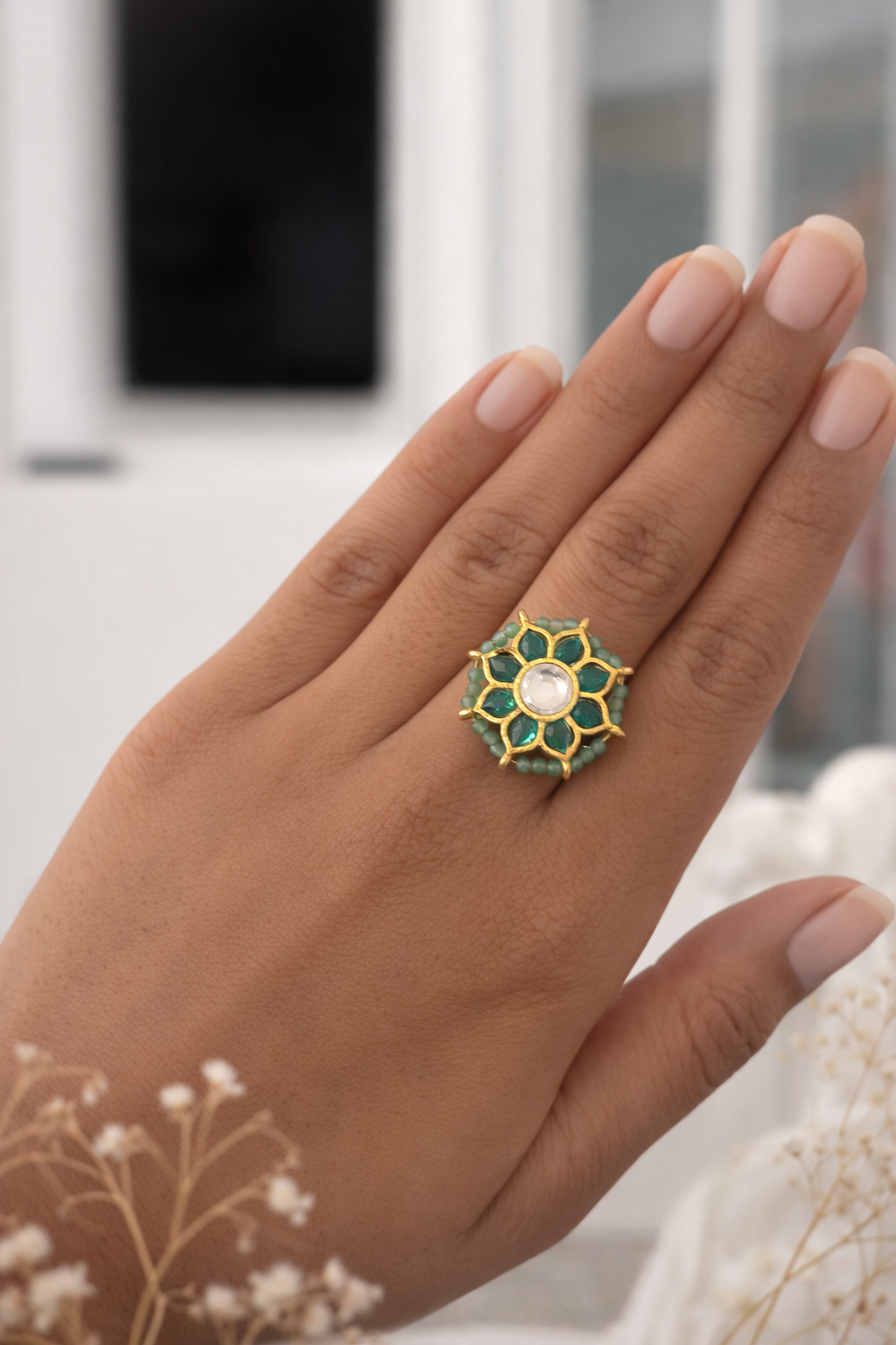 Hand wearing a decorative ring with green and gold design, blurred background