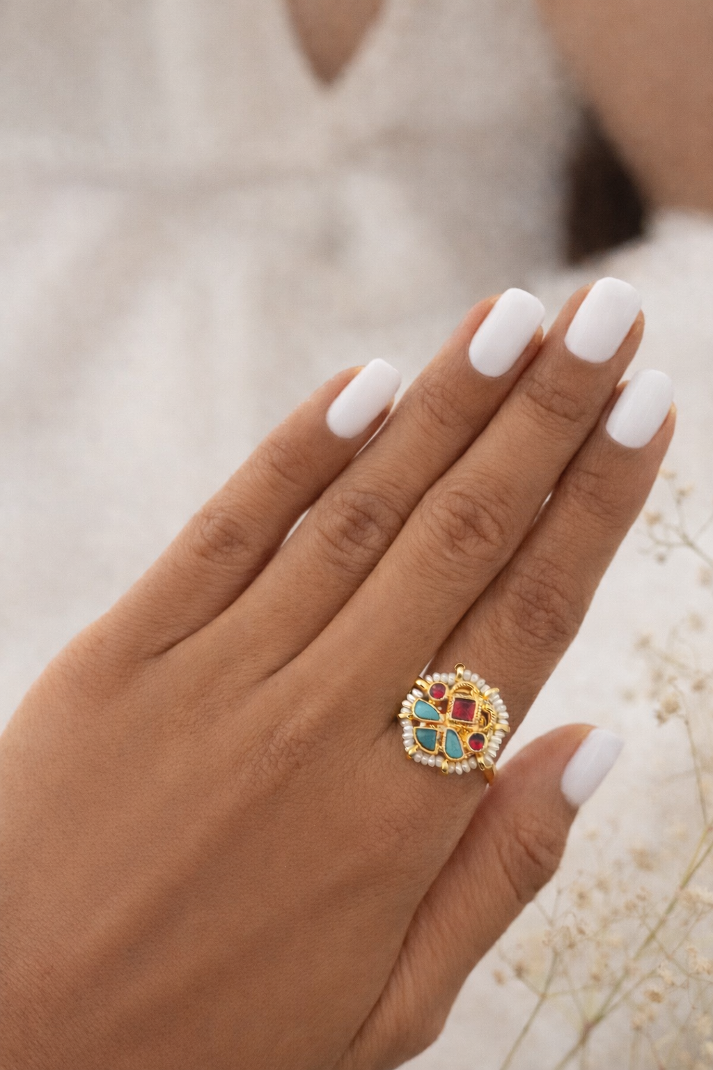Close-up of a hand wearing a decorative ring with a colorful gemstone on a neutral background