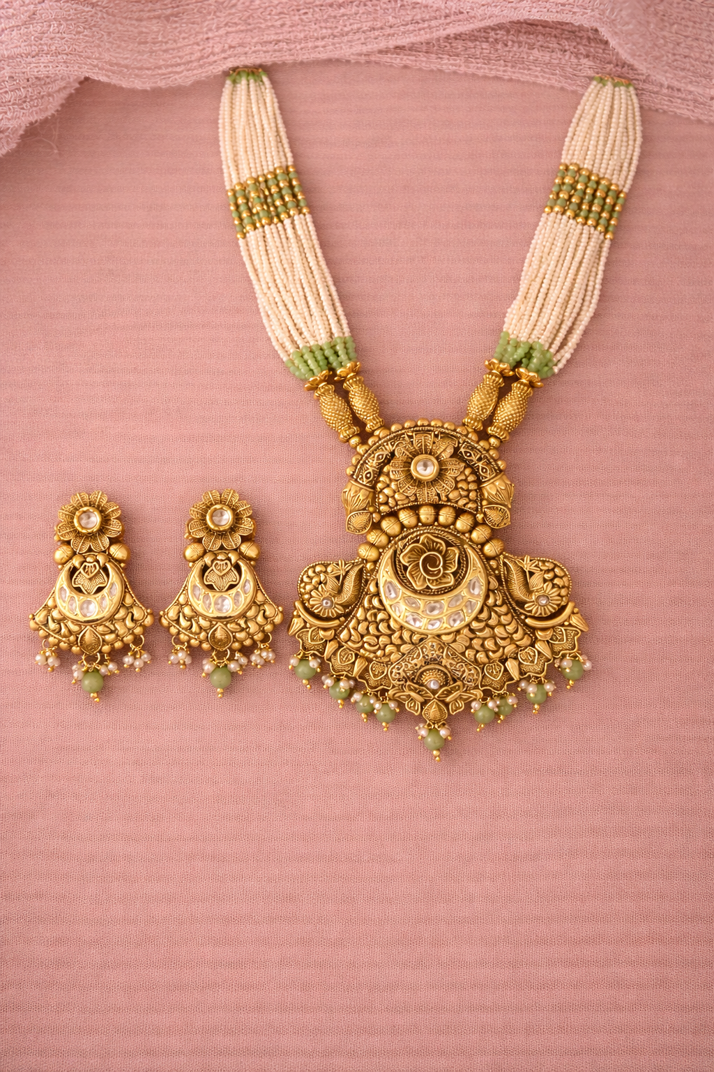 Gold necklace and earrings set on a pink background