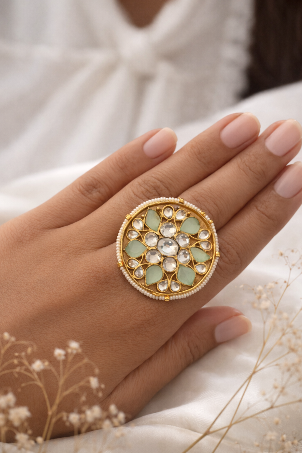 Close-up of a hand wearing a decorative ring with gemstones on a neutral background