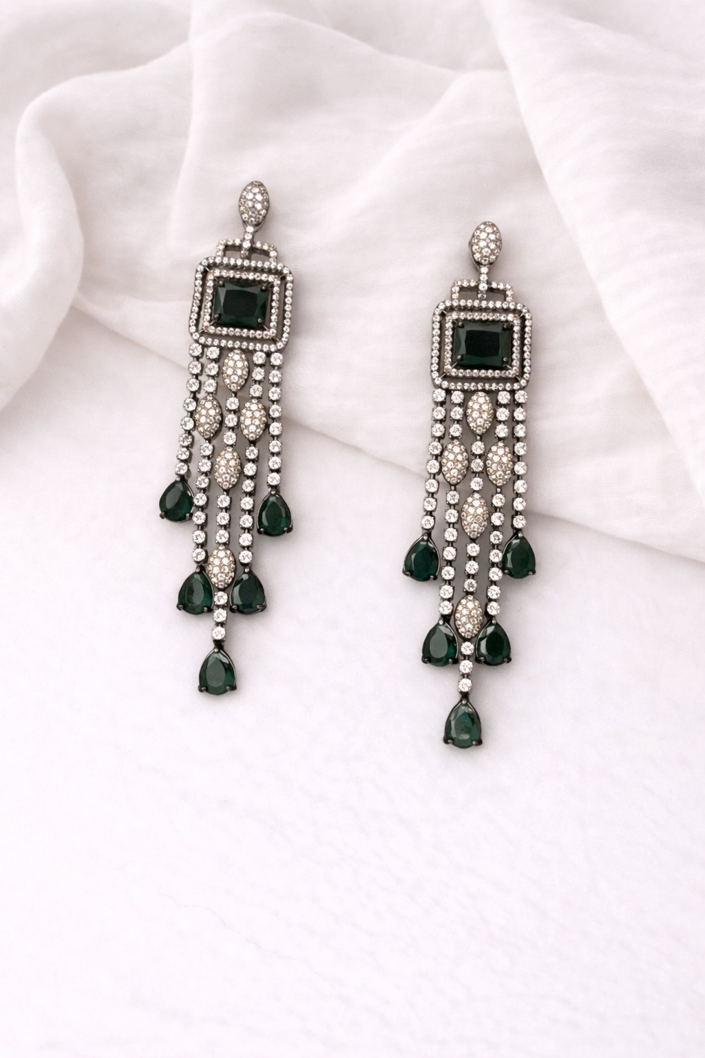 Pair of silver earrings with green gemstones on a white fabric background