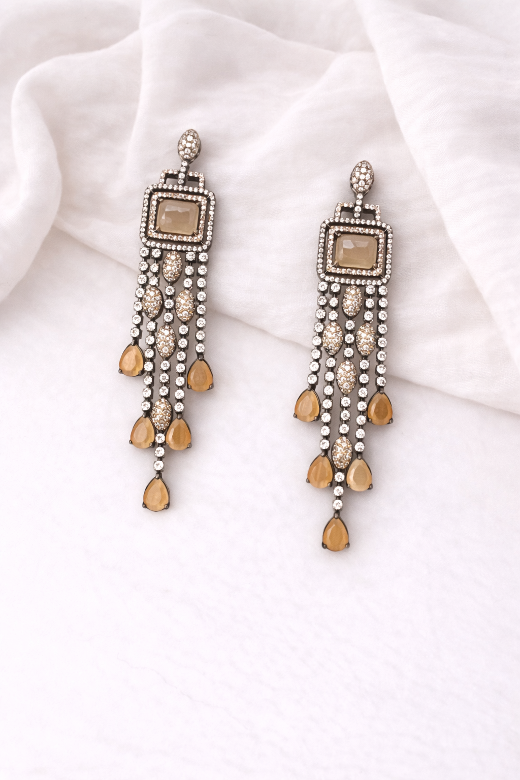 Pair of ornate earrings with beads on a white fabric background