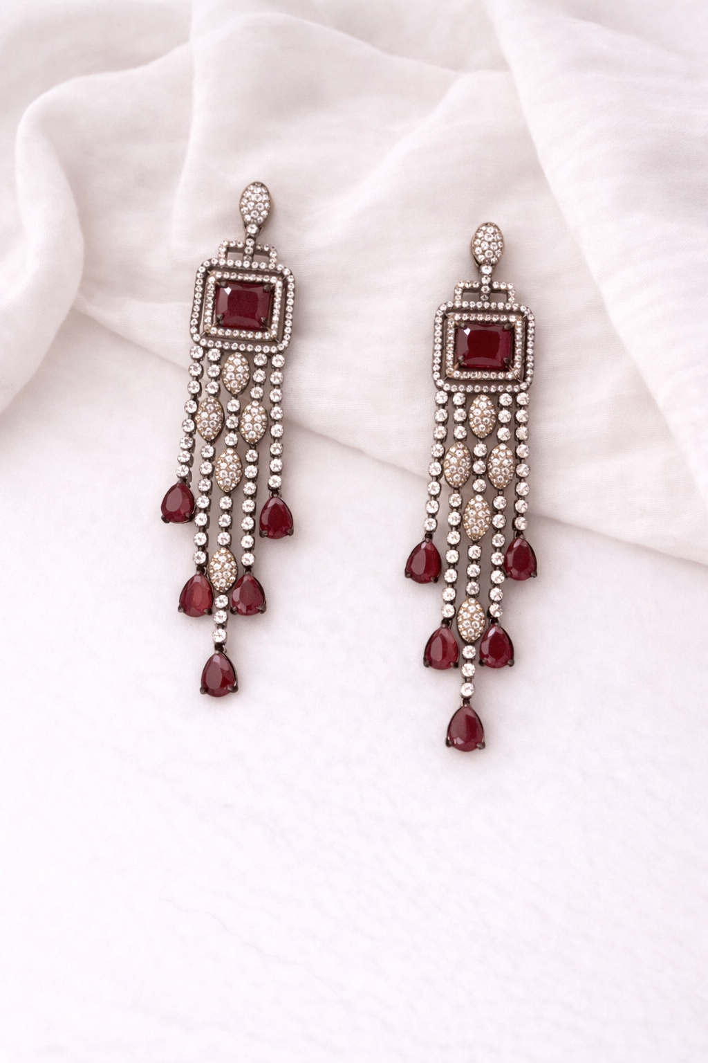 Pair of earrings with ruby gemstones and pearl-like beads on a white fabric background