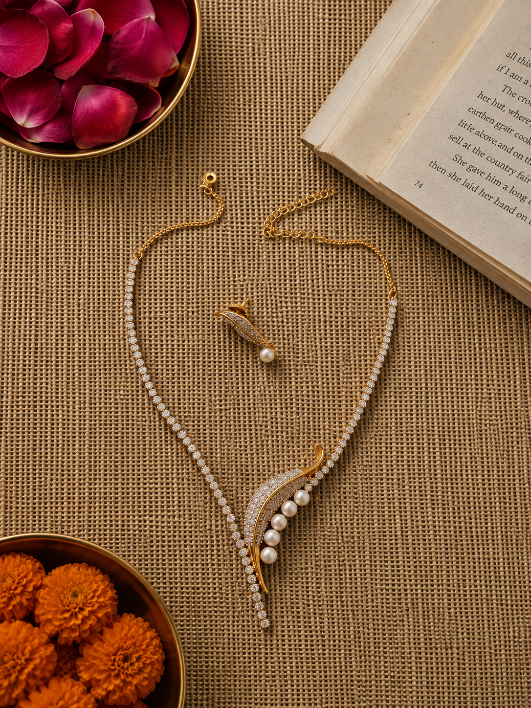 Gold-finish crystal tennis necklace featuring a leaf-inspired pearl pendant with matching crystal and pearl earrings displayed on a textured beige background.