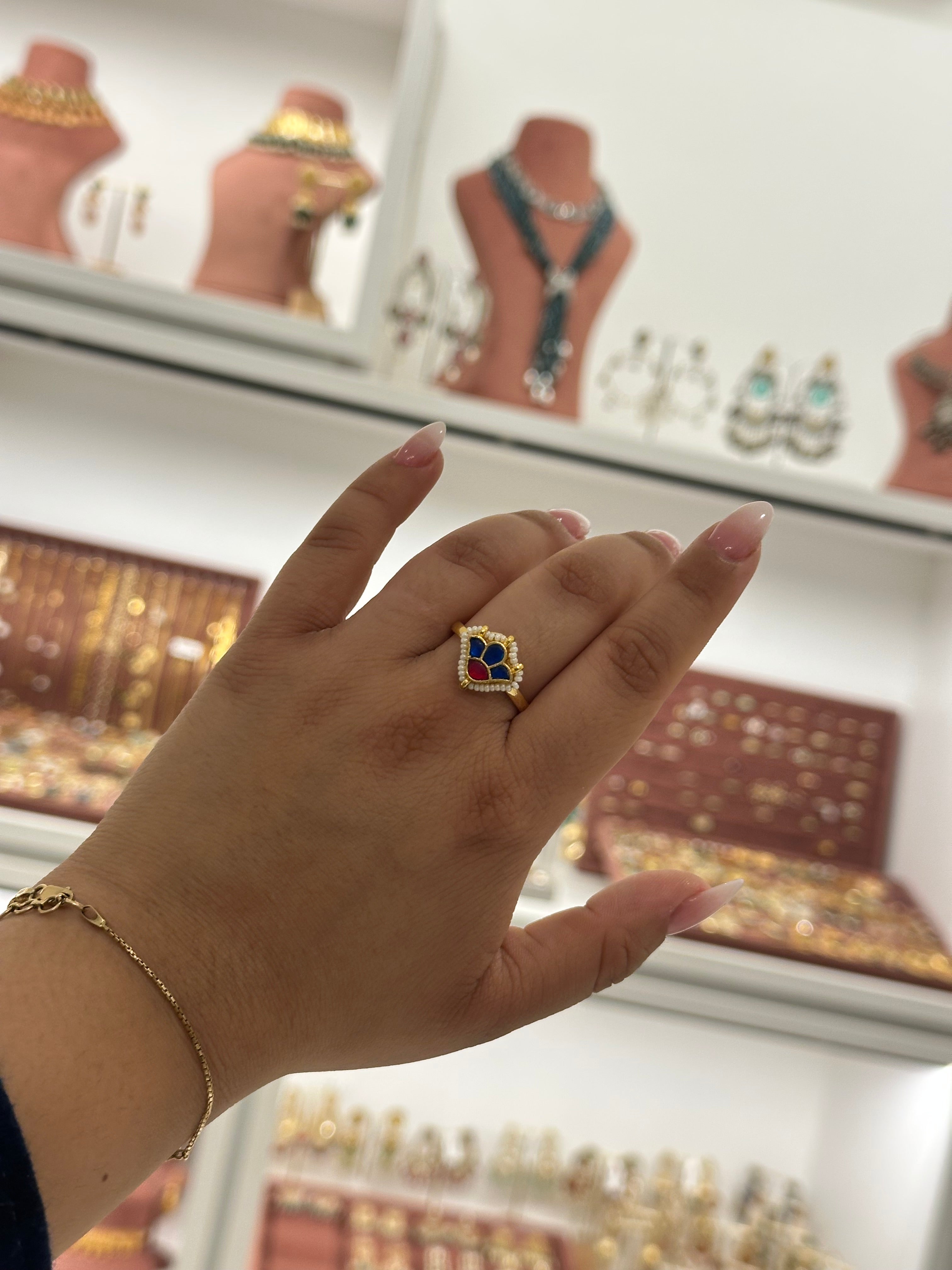 Hand wearing a gold ring with a blue gemstone in front of a jewelry display.