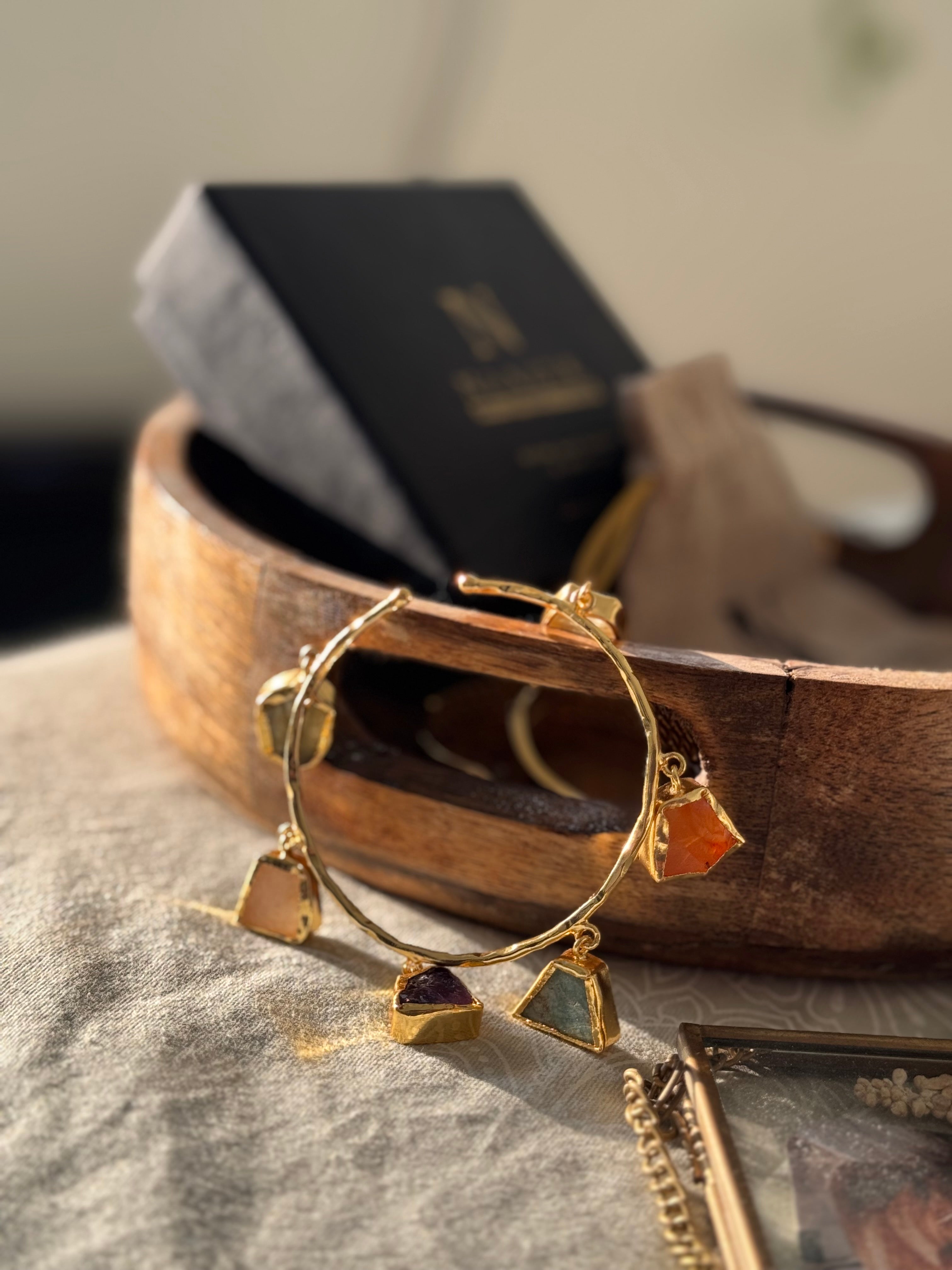 Gold bracelet with colorful stones on a textured fabric surface
