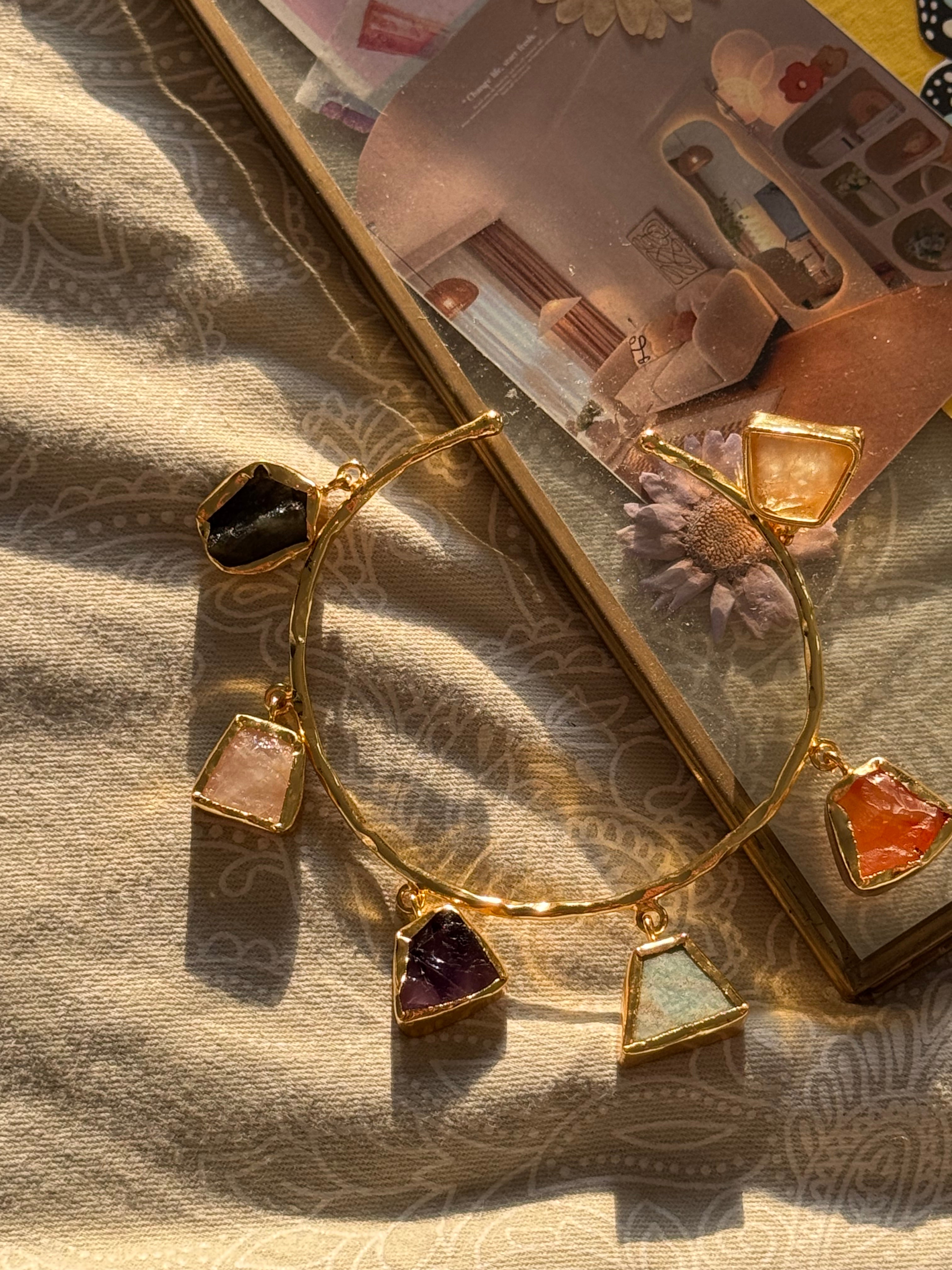 Gold bracelet with colorful stones on a textured fabric surface