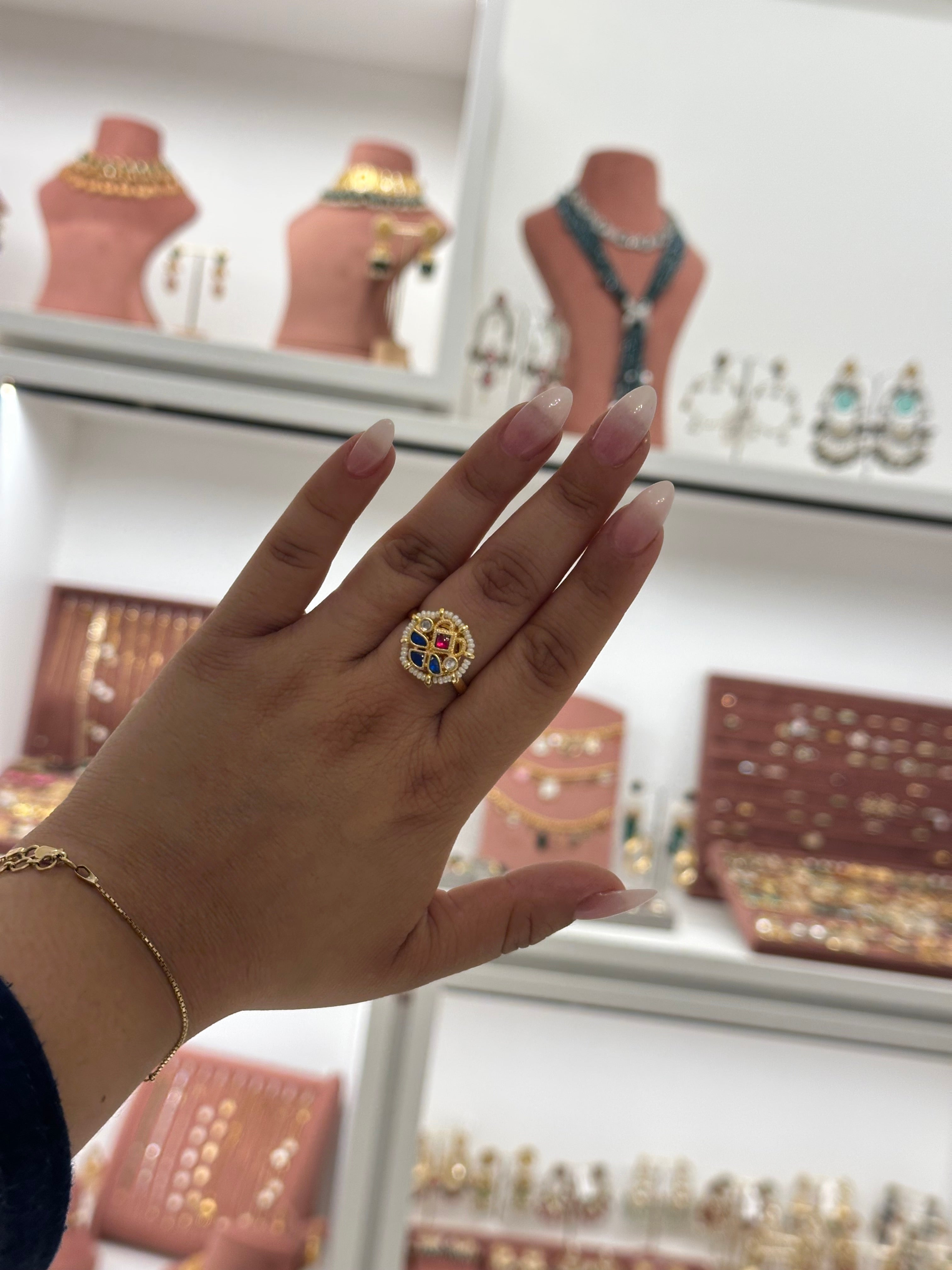 Hand wearing a gold ring with a blue gemstone, set against a background of jewelry displays.