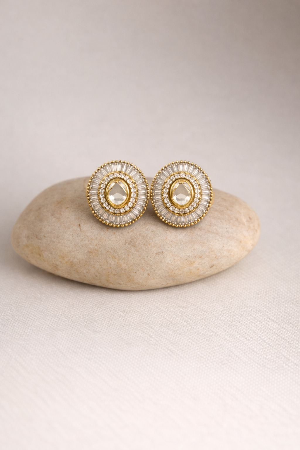 Pair of gold and pearl earrings on a beige stone