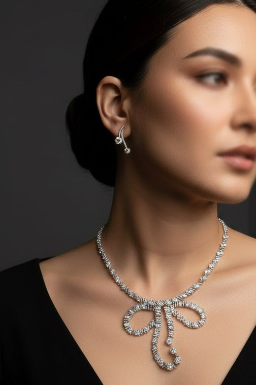 A close-up of a person wearing a silver-toned ear cuff earring, holding the matching earring in their hand to show its details. The person is wearing a black t-shirt with silver rhinestone trim.