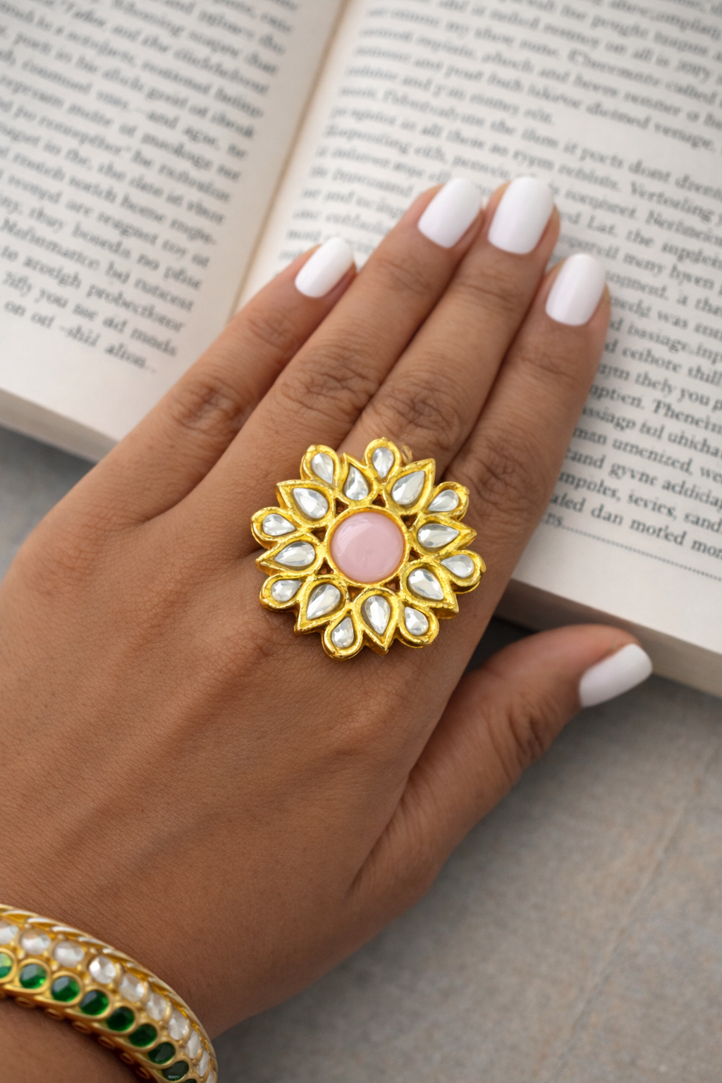 Hand wearing a gold and pink ring with an open book in the background